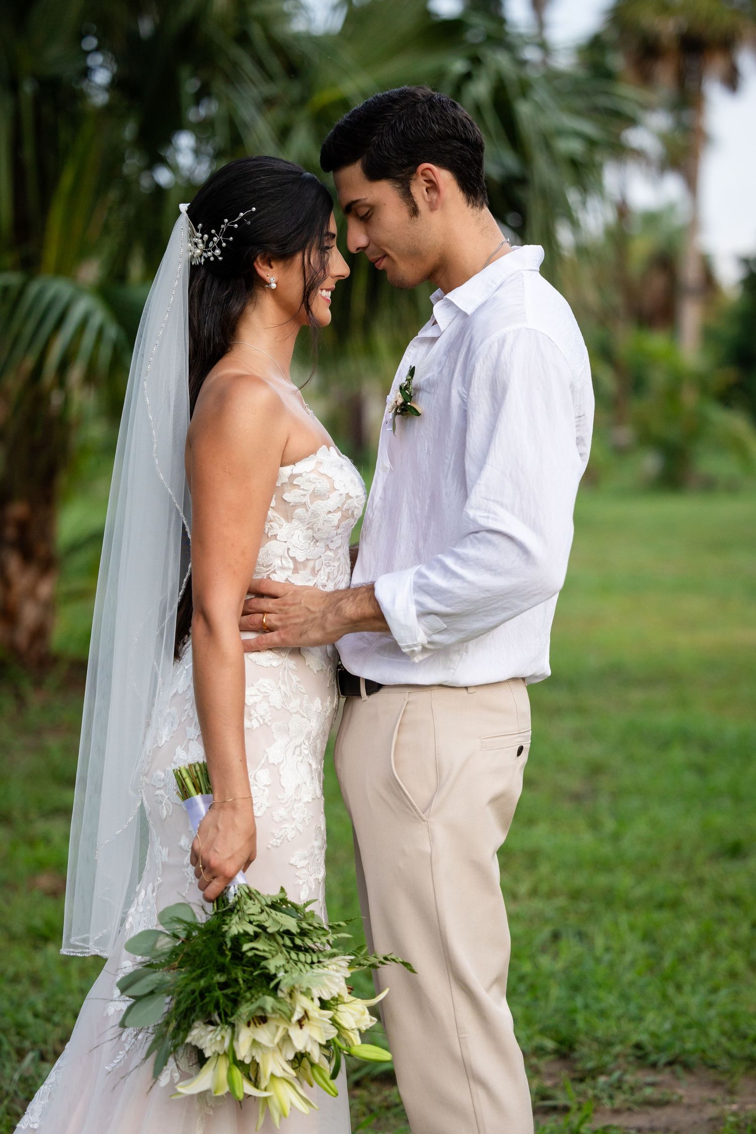 Newlyweds share intimate moments in a lush tropical garden setting while the bride holds a green bouquet.