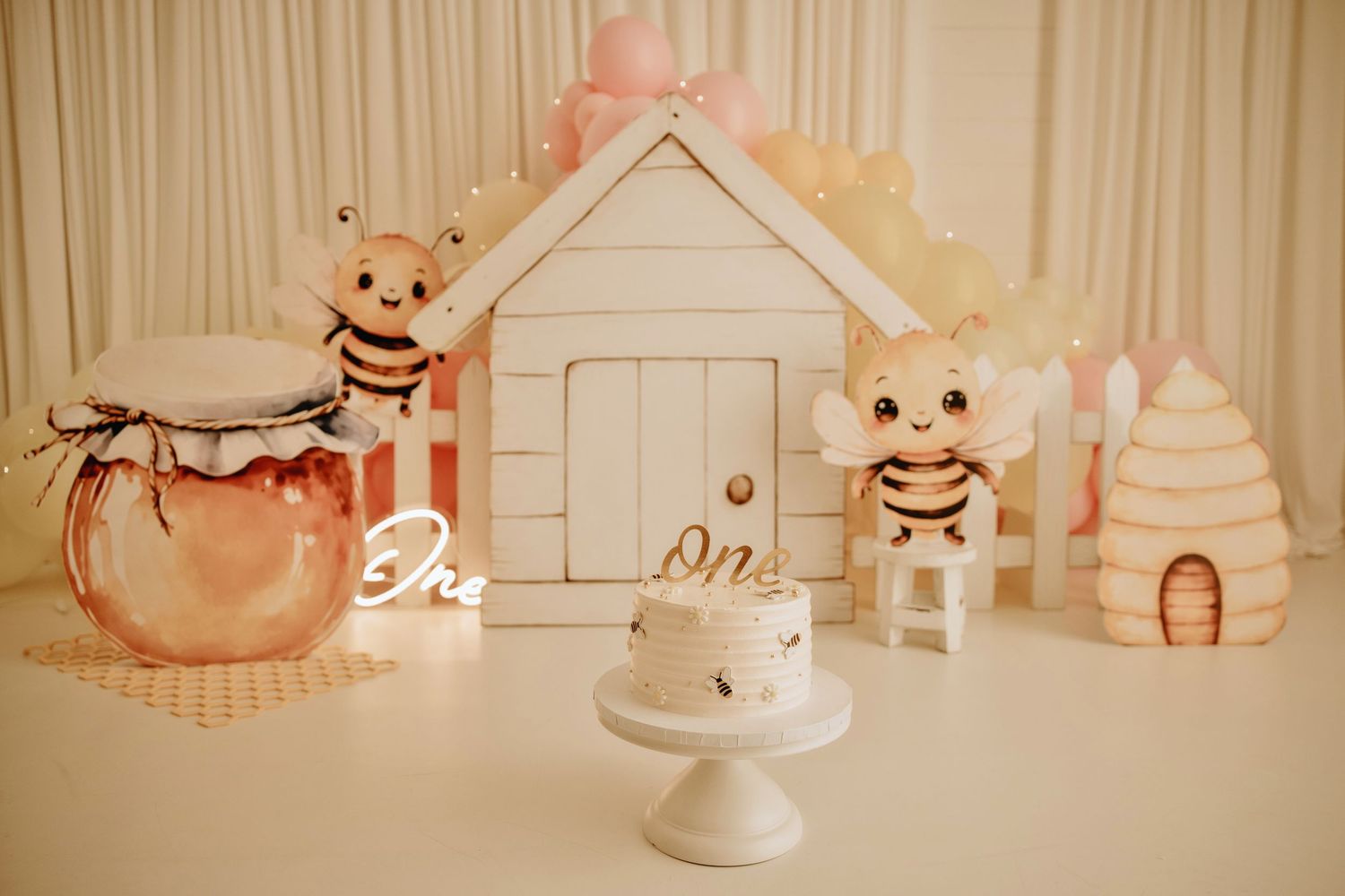 Adorable bee-themed first birthday cake smash setup with honey jar, beehive decorations, and a small white cake.