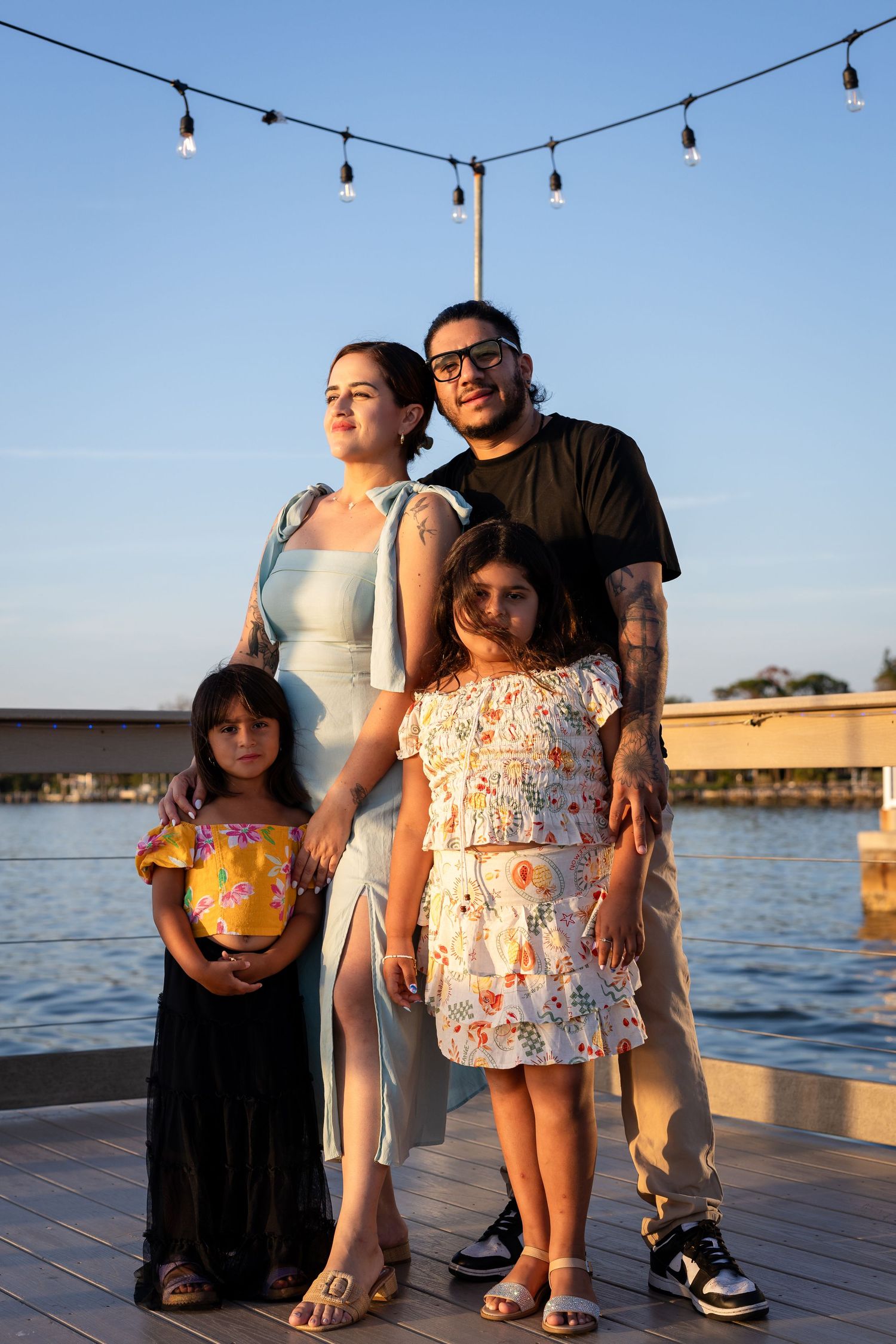Waterfront family portrait with string lights and sunset backdrop.
