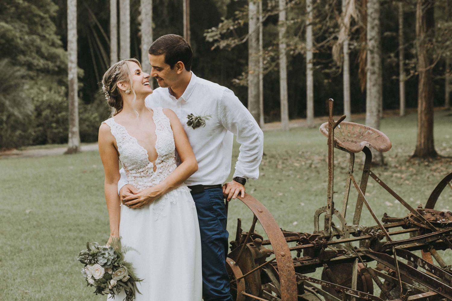A romantic moment between newlyweds in a rustic forest setting with vintage farm equipment.