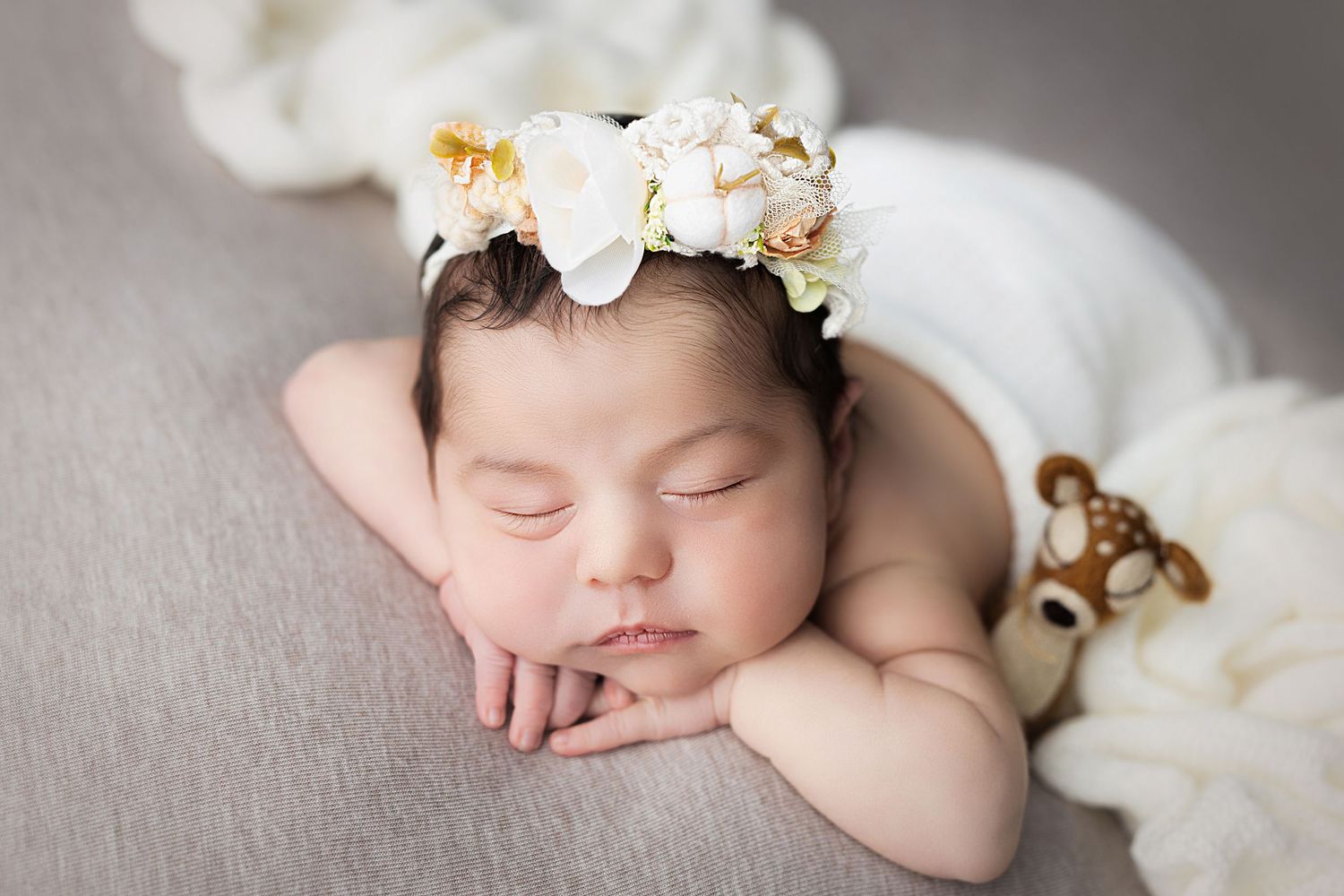 Sleeping newborn wearing delicate floral crown on grey background.