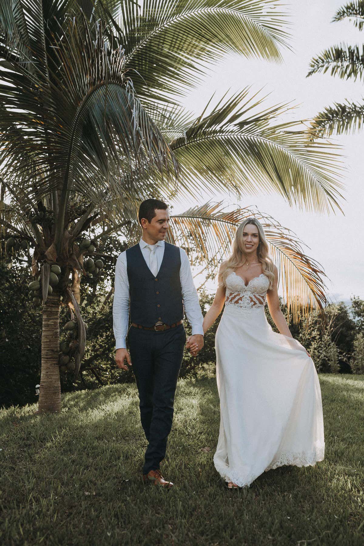 Bride and groom walking hand in hand under palm trees in this fotografia de bodas en Tampa.