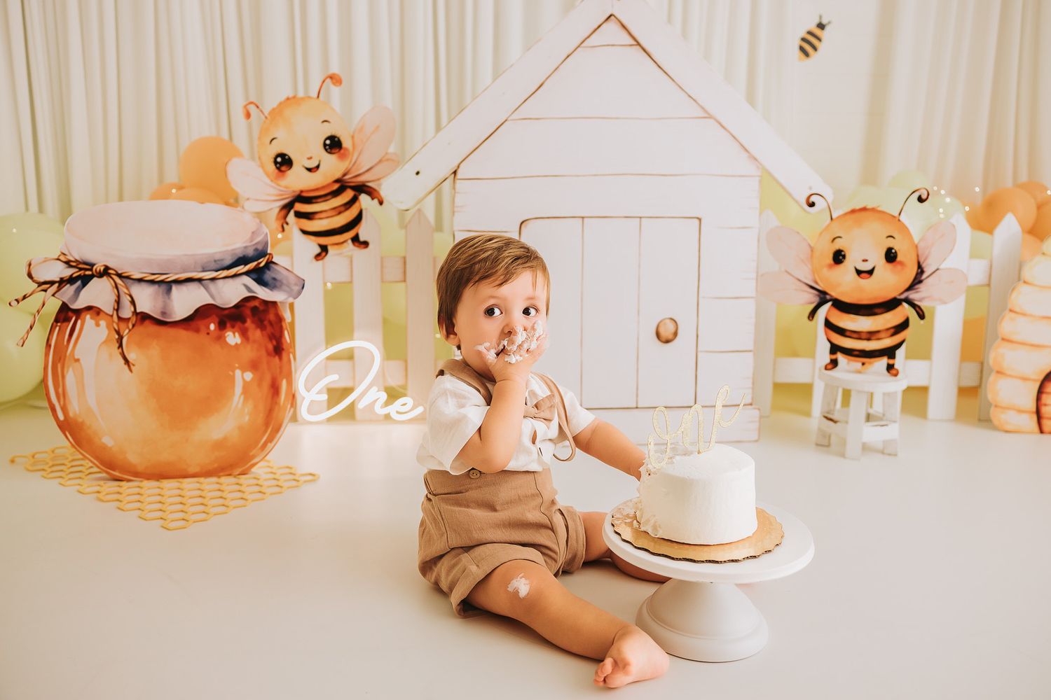 Baby's first birthday cake smash with bee theme decorations, honey pot, and white house backdrop.