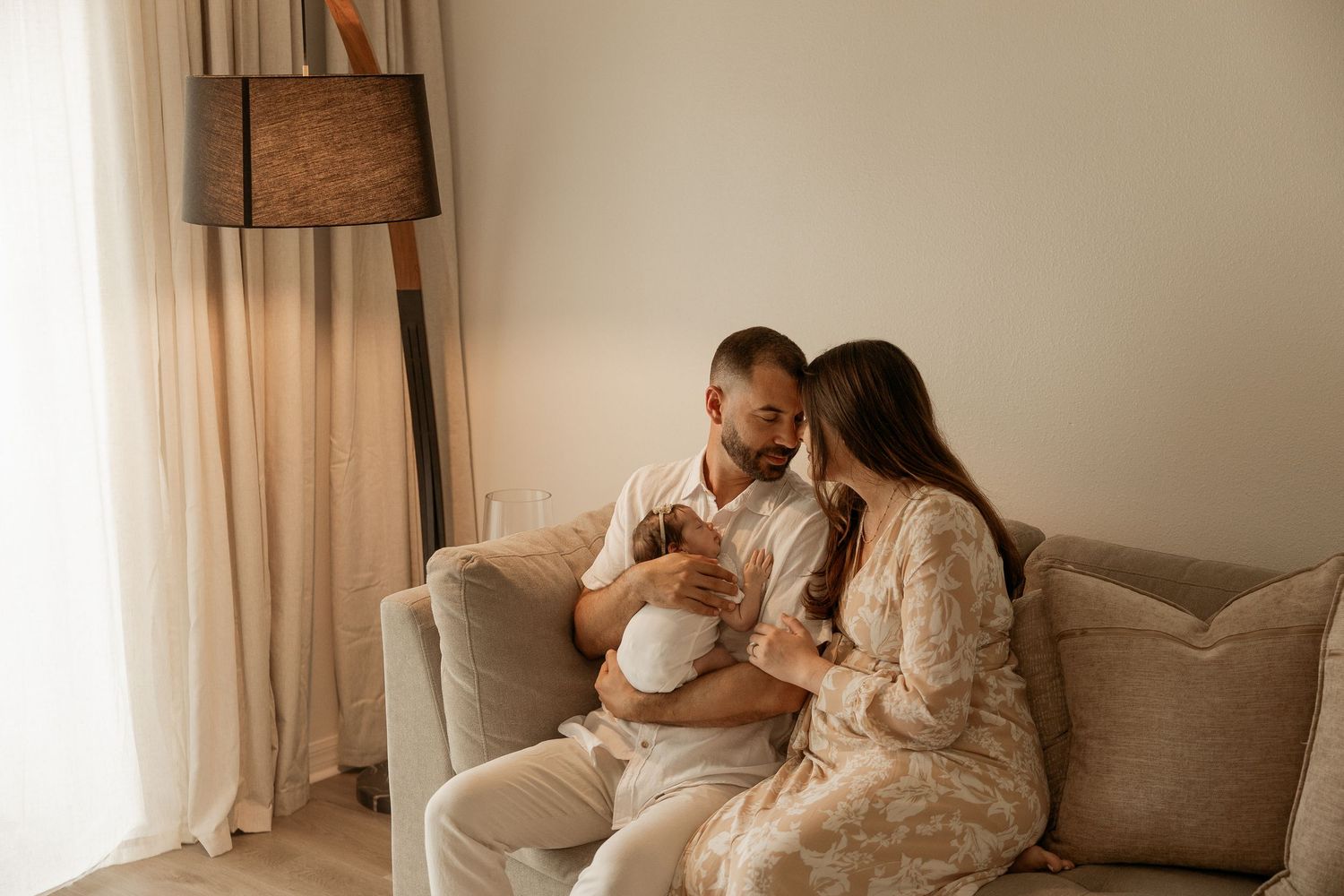 A couple sitting on a cozy sofa, lovingly cradling their newborn baby in a warm, softly lit living room.