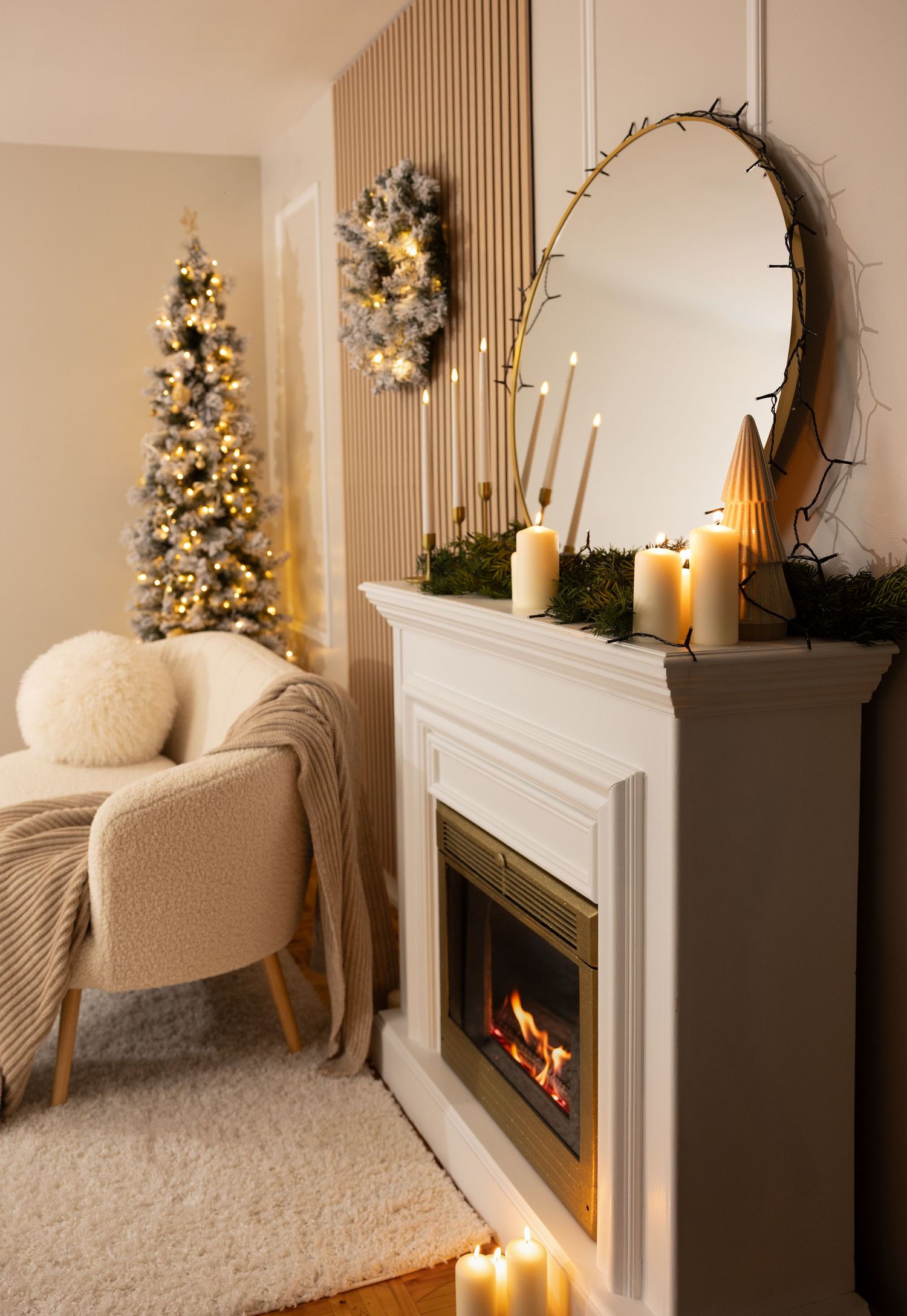 Cozy Christmas living room with lit fireplace, candles on mantel, round mirror, and decorated tree in corner.