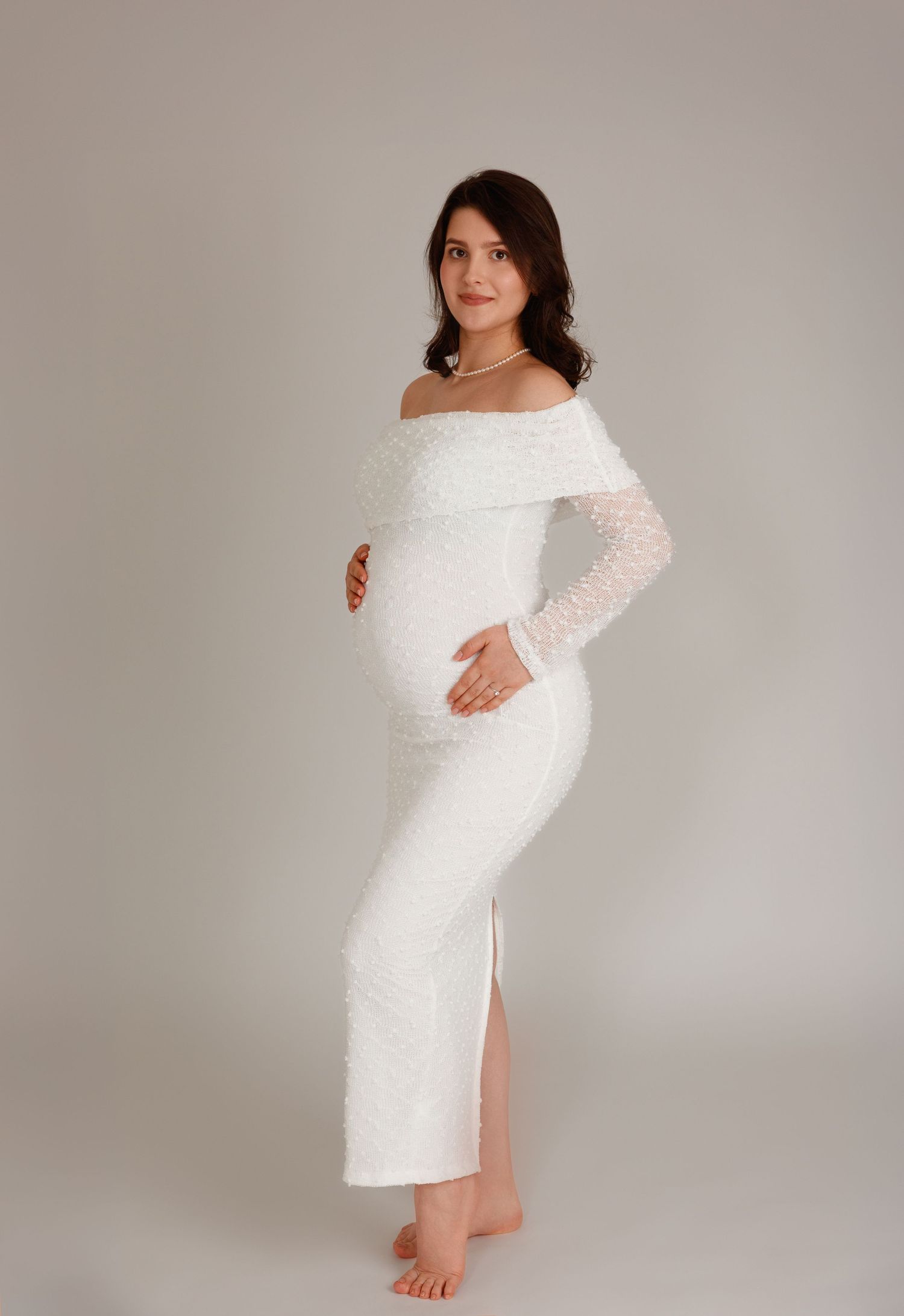 Maternity photography in Laval — pregnant woman in a white off-shoulder lace gown in a bright studio.