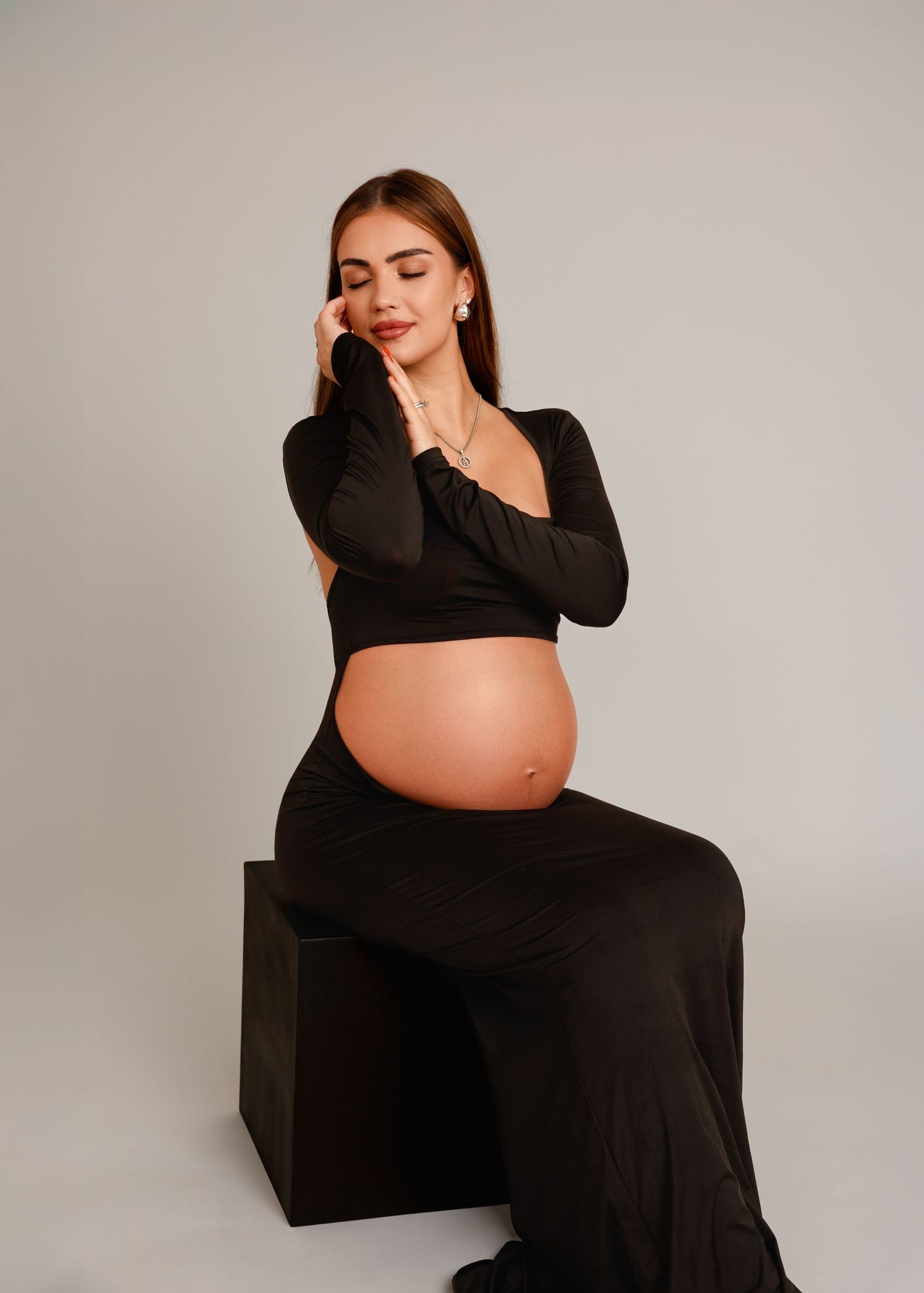 Maternity photography in Laval, Montréal — pregnant woman in a black crop top and skirt seated on a cube.