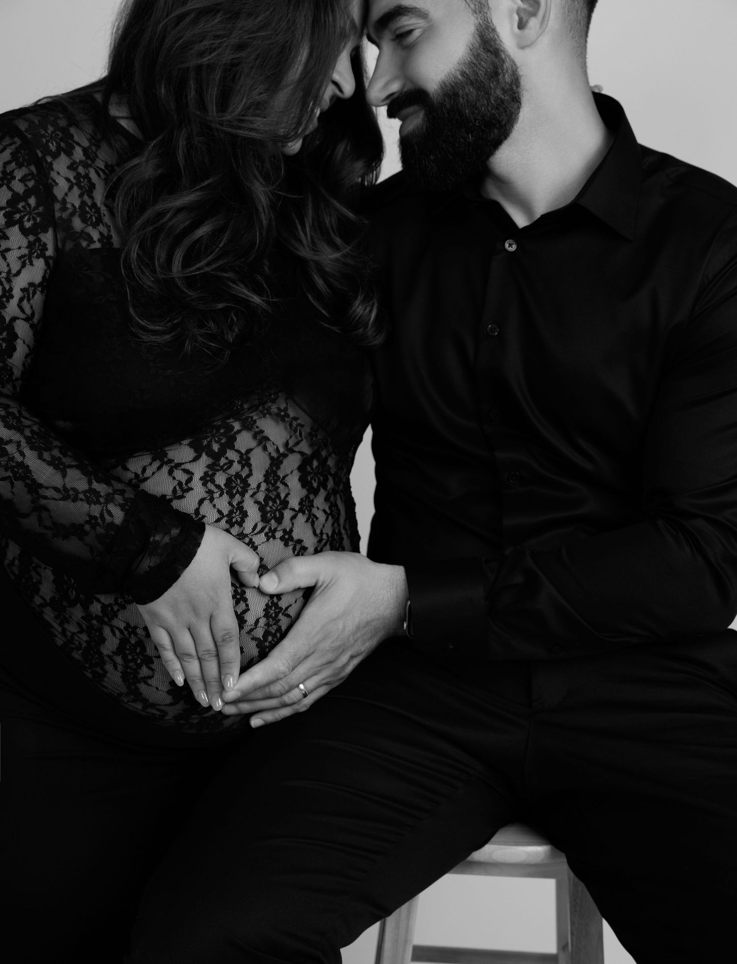 Black-and-white maternity photography in Laval — couple forming a heart with their hands on the baby bump.