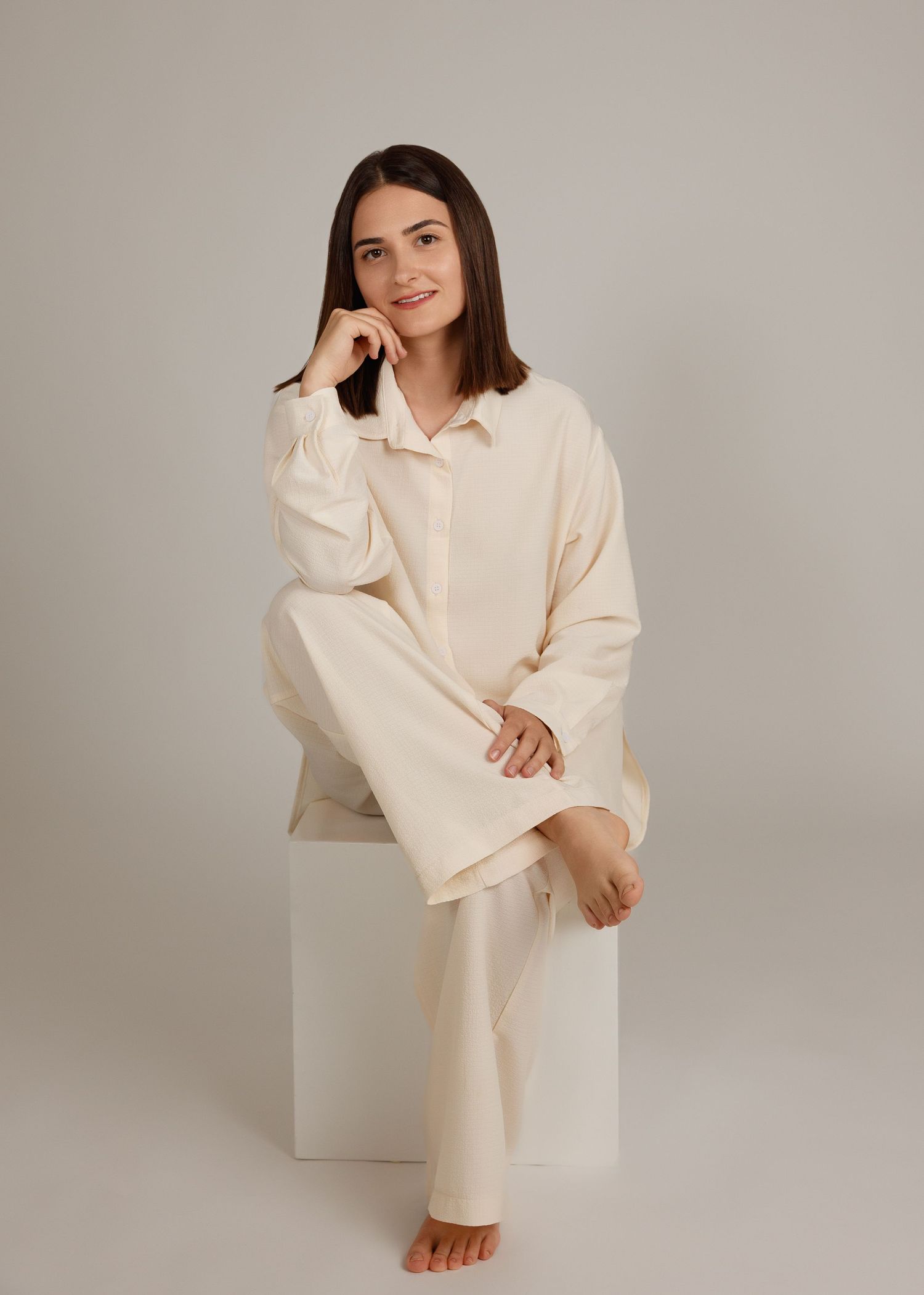 Portrait photography in Laval — woman in a cream oversized shirt seated on a white cube.