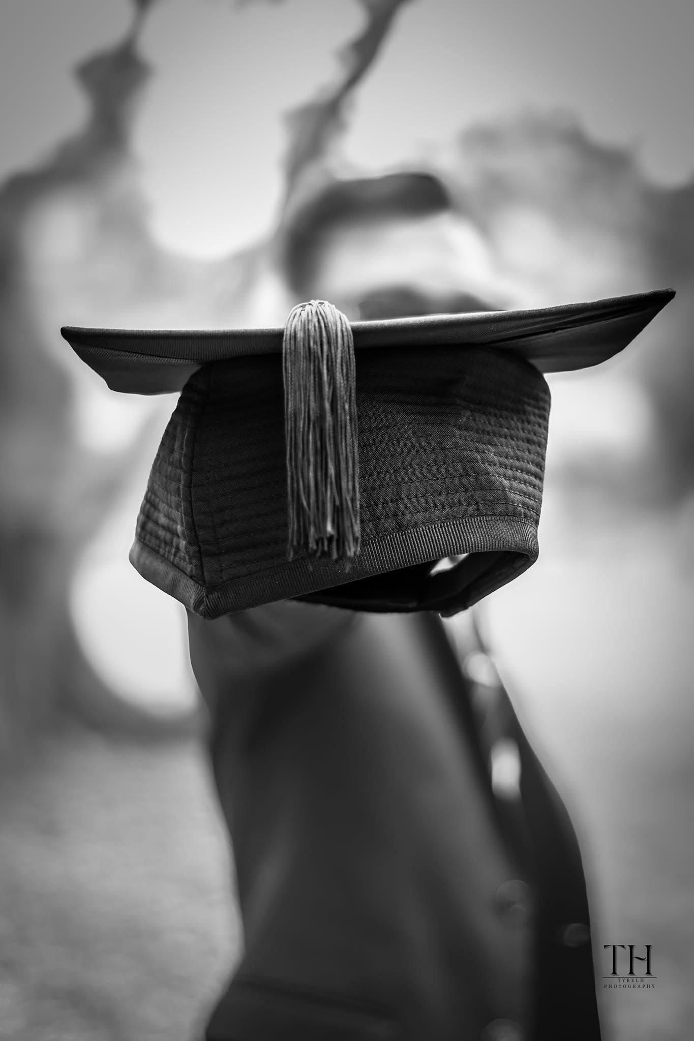Black and white photo of a graduation cap with tassel, resting on a surface with blurred background.
