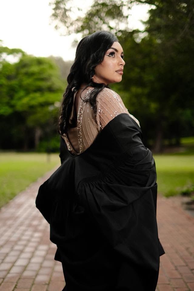 A woman in a black saree with embellished blouse poses elegantly on a brick path in a lush green park.
