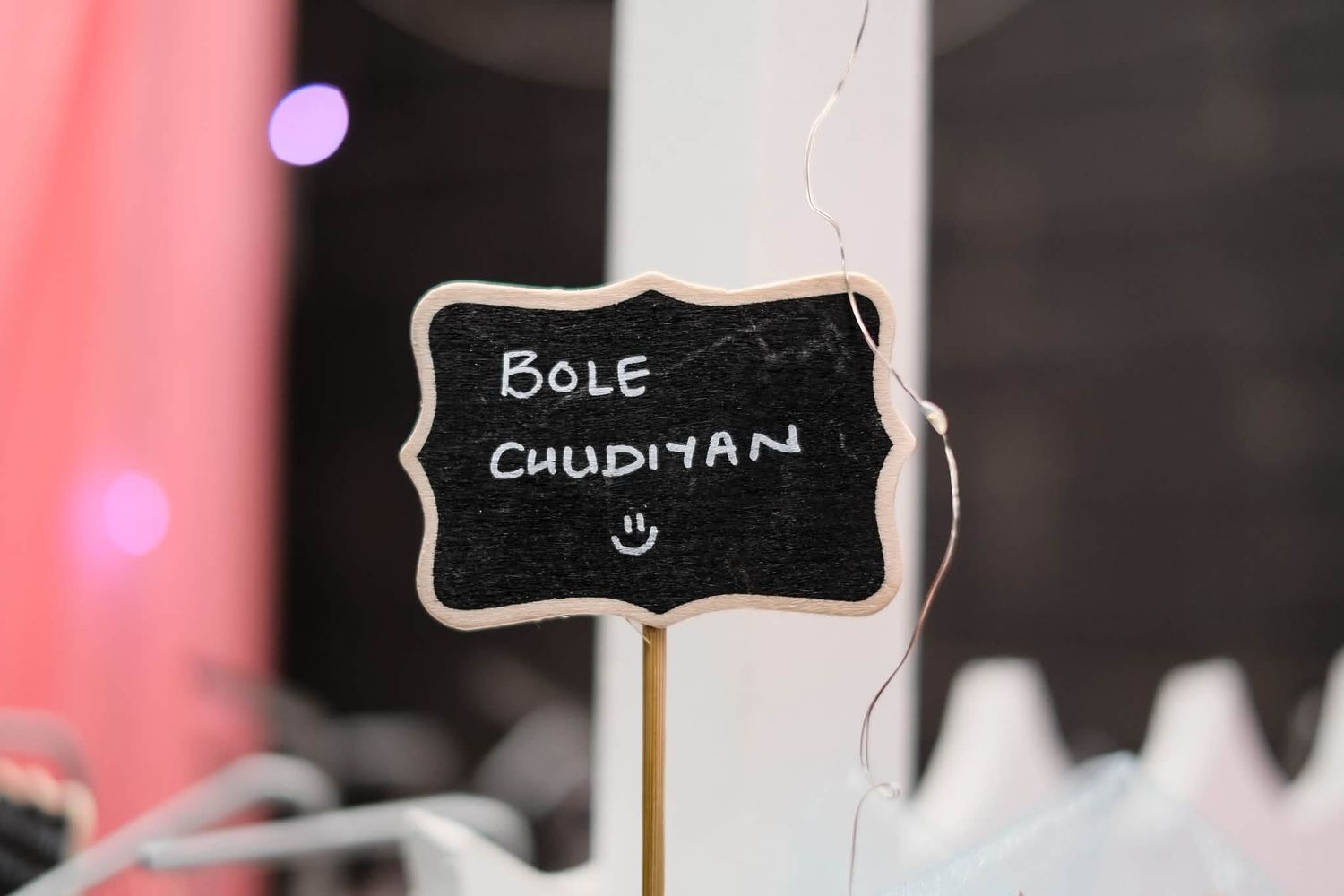 A decorative chalkboard sign reading Bole Chudiyan displayed on a wooden stake at an event.