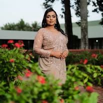 Woman in elegant beige embroidered dress posing in a lush garden with red flowers.
