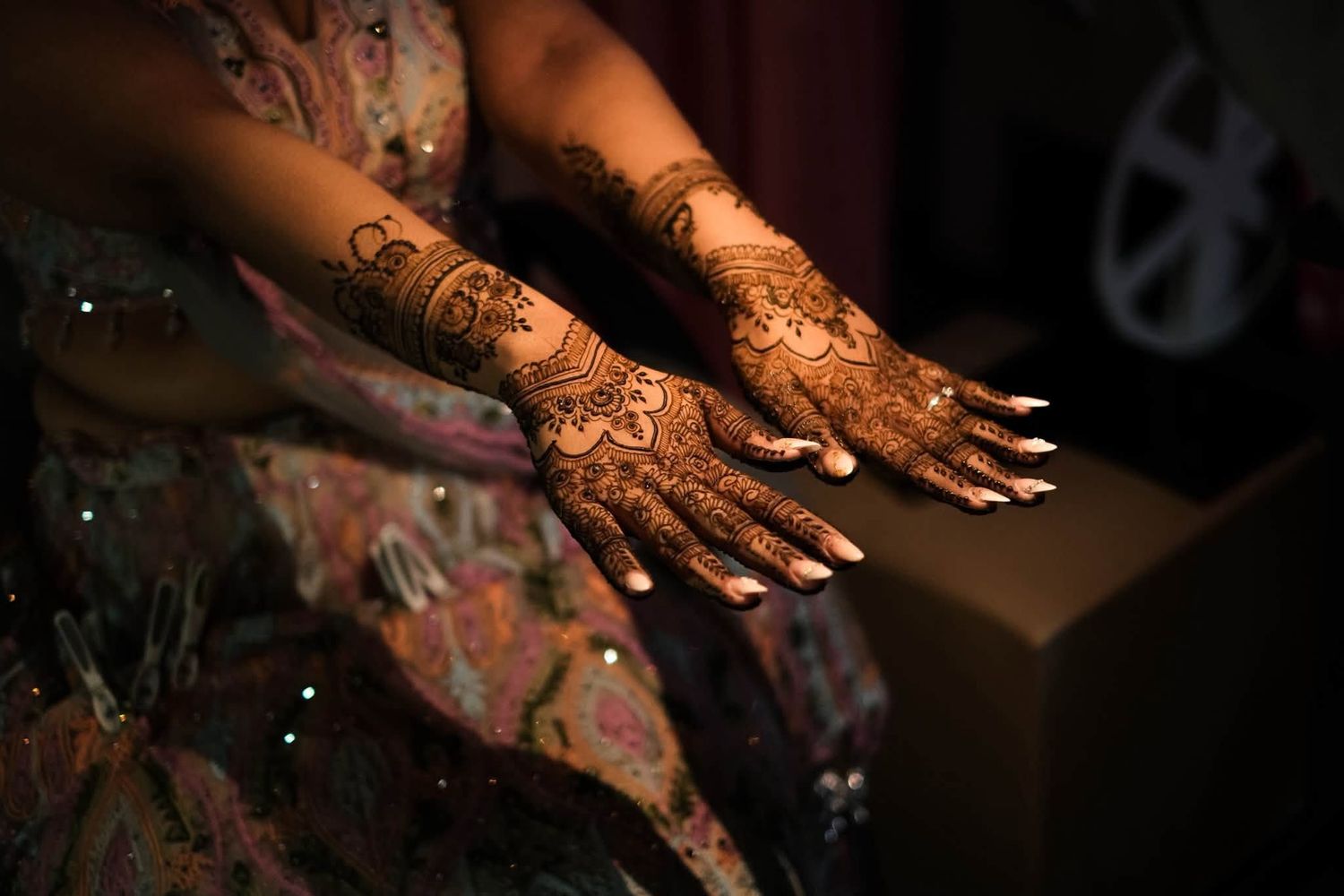 Close-up of intricate henna mehndi designs on a bride's hands and forearms at a traditional wedding.