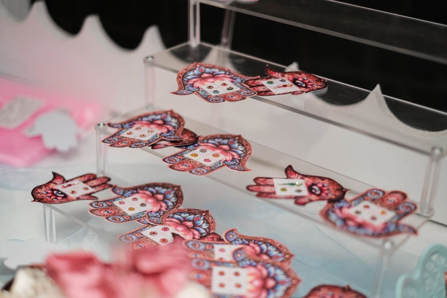 Decorative Hamsa hand-shaped cookies with colorful paisley patterns displayed on clear acrylic tiered tray.