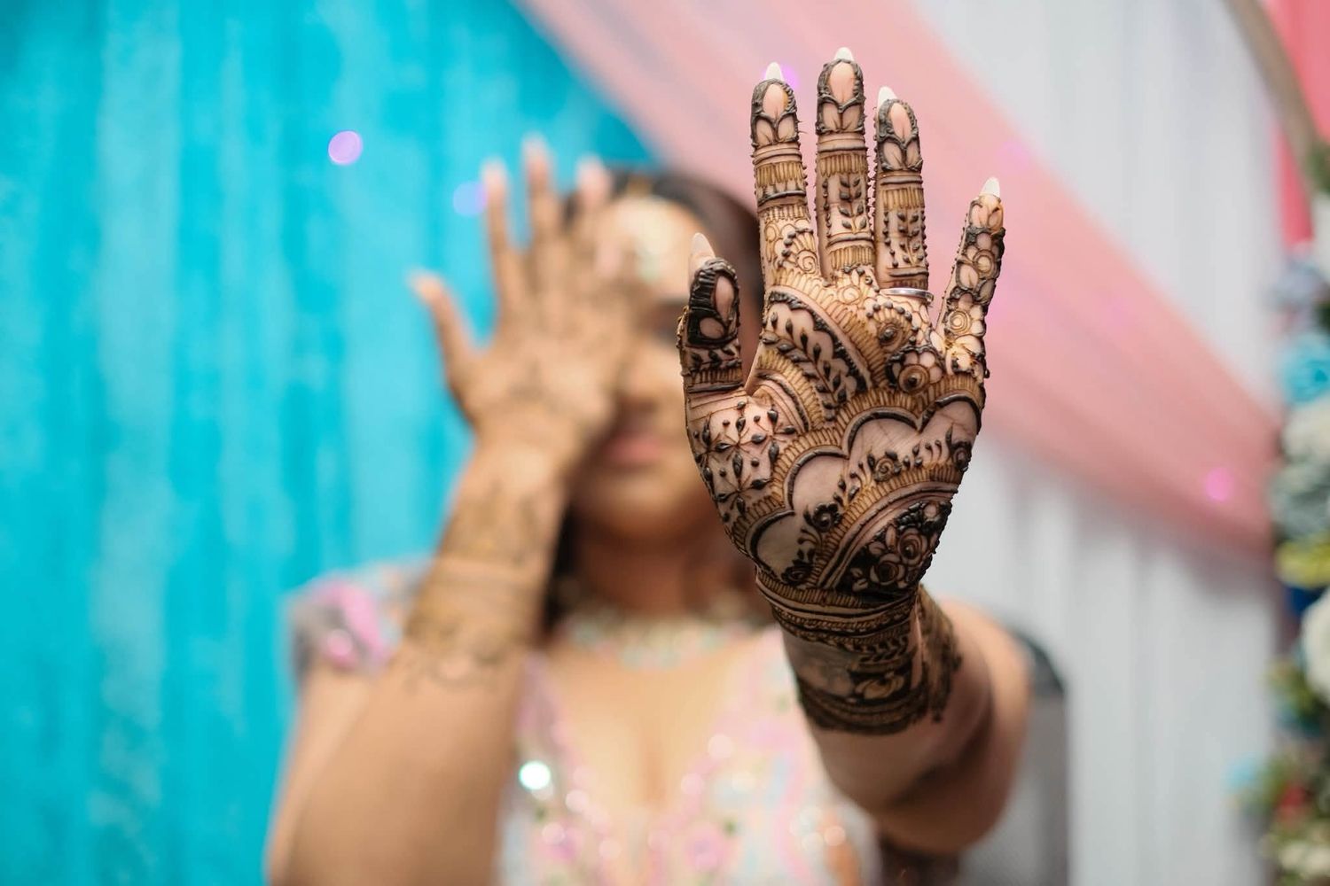 Woman displaying intricate henna mehndi design on her hand at a traditional Indian wedding celebration.