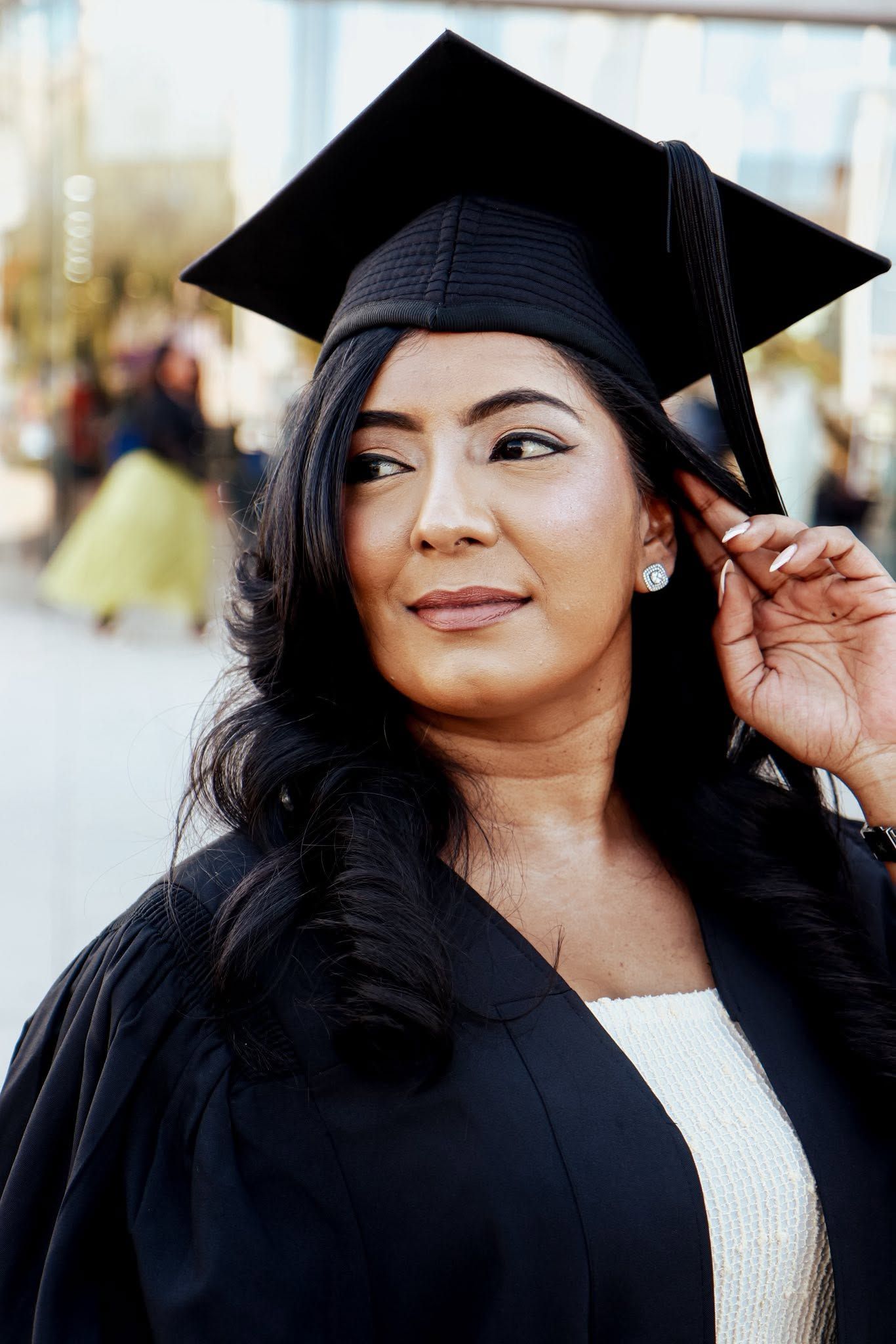 Young woman in black graduation cap and gown smiling outdoors on her graduation day.
