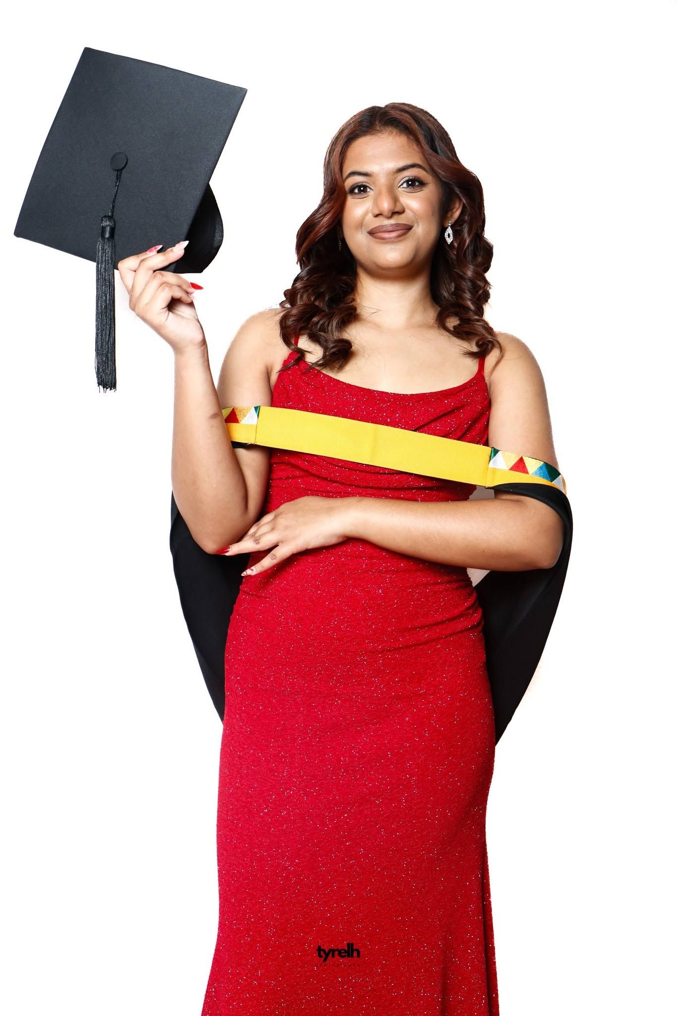 Young woman in red dress holding graduation cap and wearing academic sash, smiling against white background.