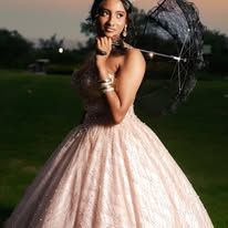 Young woman in a sparkling blush ball gown holding a black lace parasol outdoors at dusk.
