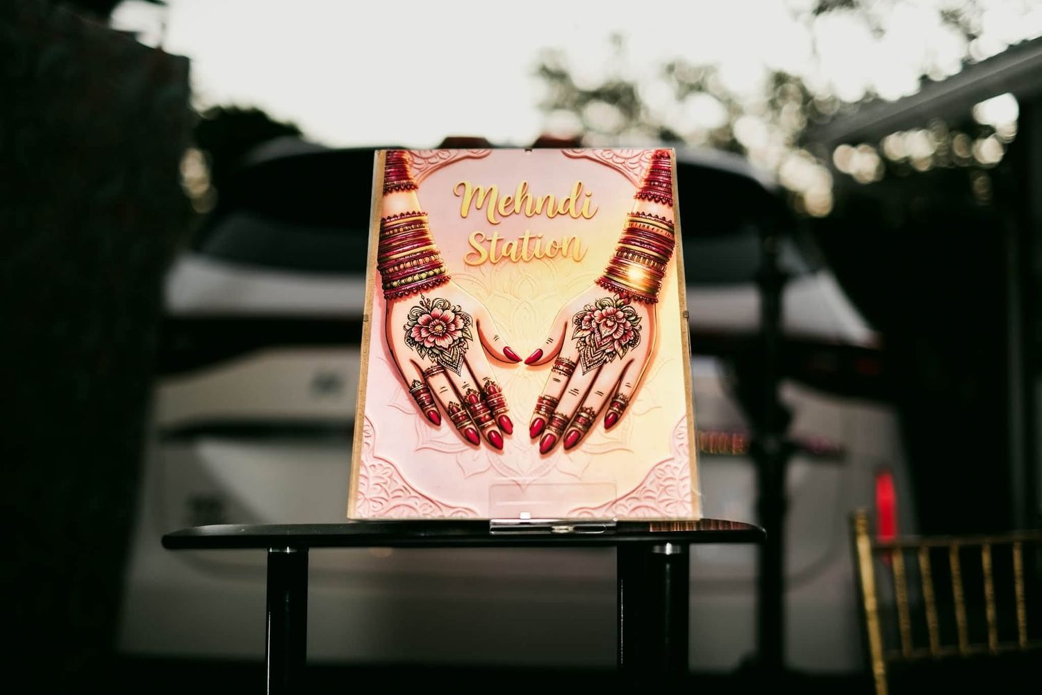 Illuminated Mehndi Station sign with henna-decorated hands design at an Indian wedding celebration.