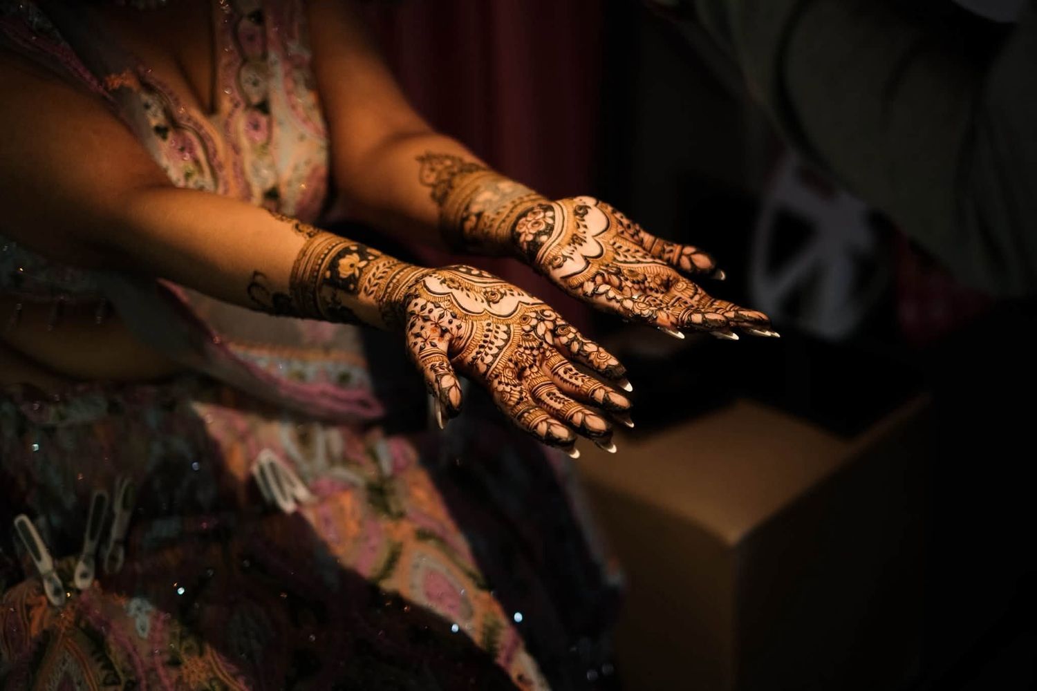 Woman displaying intricate henna mehndi designs on both hands, featuring traditional floral and paisley patterns with decorative accents.