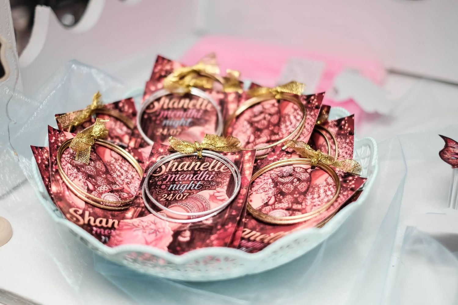 Pink personalized wedding favor medals with gold ribbon displayed in a decorative blue bowl at a celebration event.