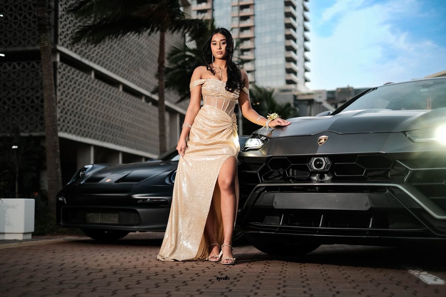 Woman in elegant gold slit gown posing beside a black Lamborghini Urus SUV in an urban setting.