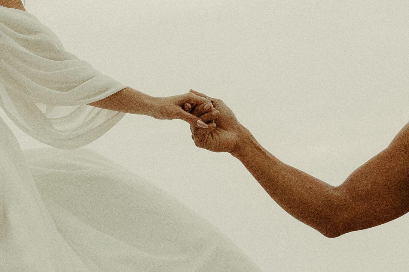 Close-up of bride and groom holding hands, white fabric flowing in the breeze.