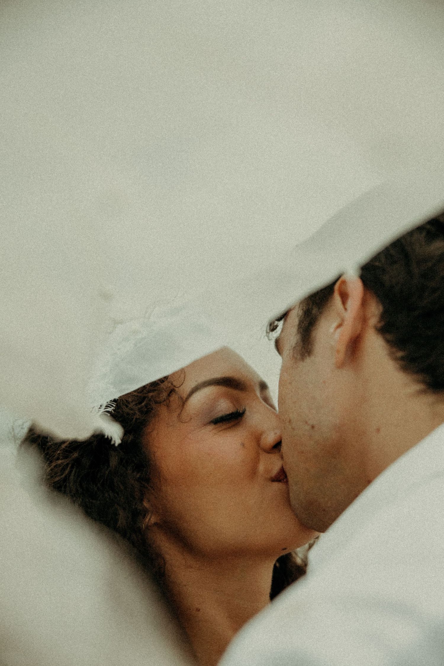 Close-up of couple sharing a romantic kiss under a white wedding veil.