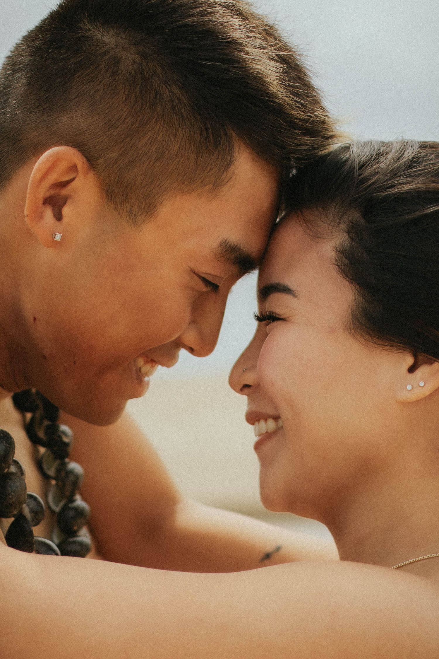 Close up of smiling Asian couple touching foreheads tenderly on a sunny beach.
