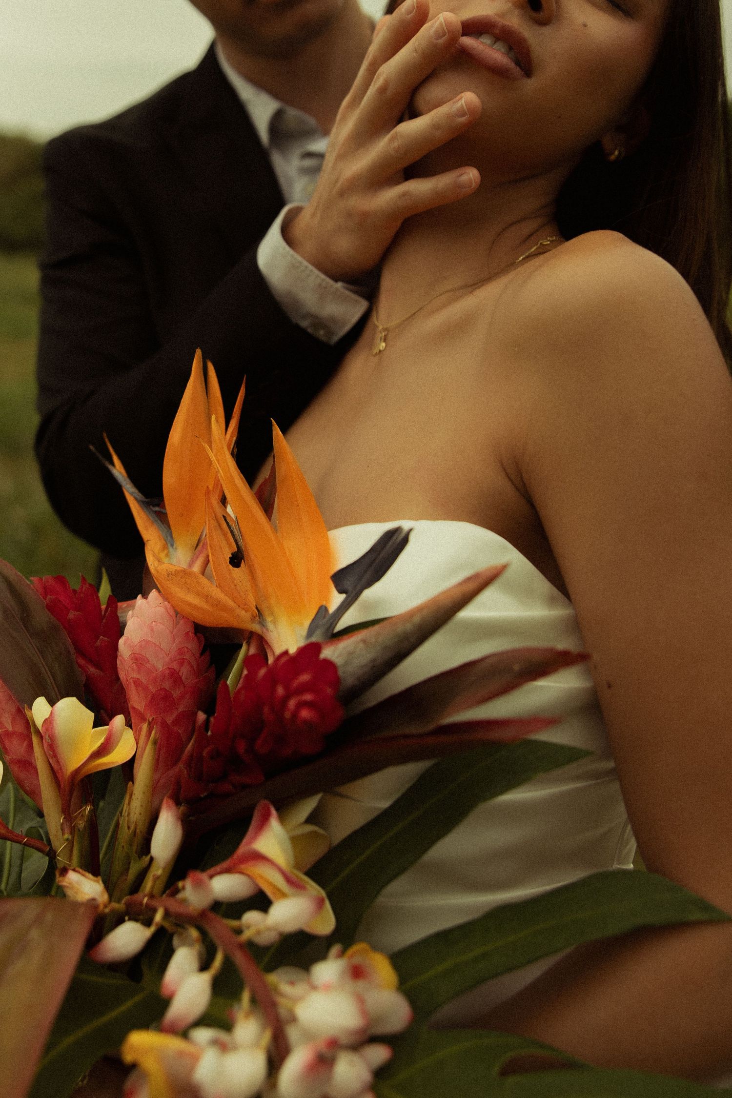 Groom gently touching bride's face as she holds a vibrant tropical wedding bouquet.