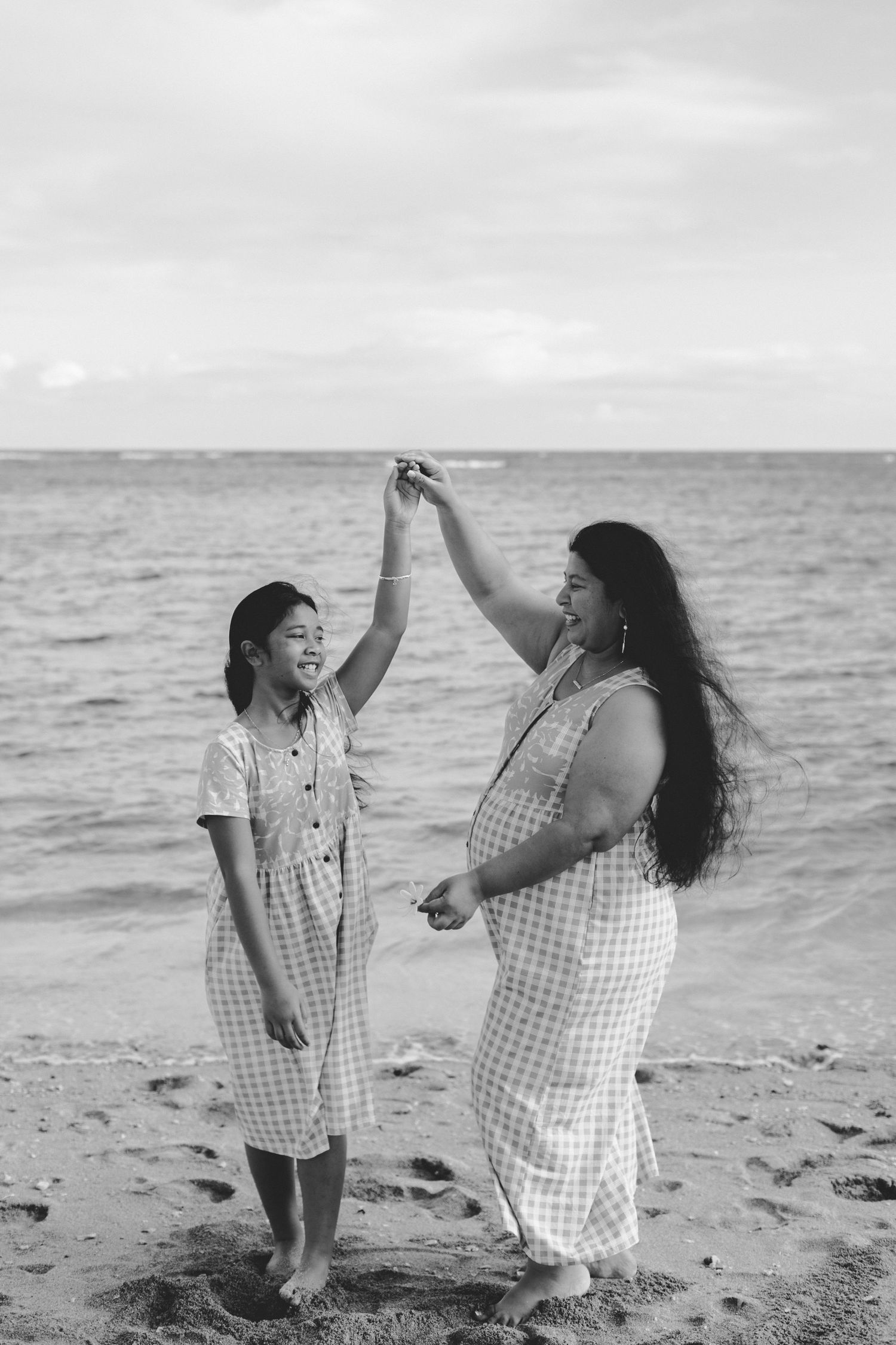 Black and white photo of mother and daughter dancing together on a beach by the ocean.