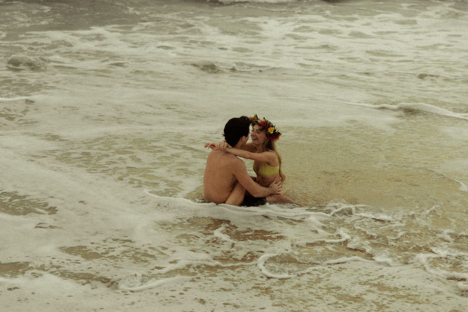 Couple embracing in ocean waves, woman wearing a floral crown.