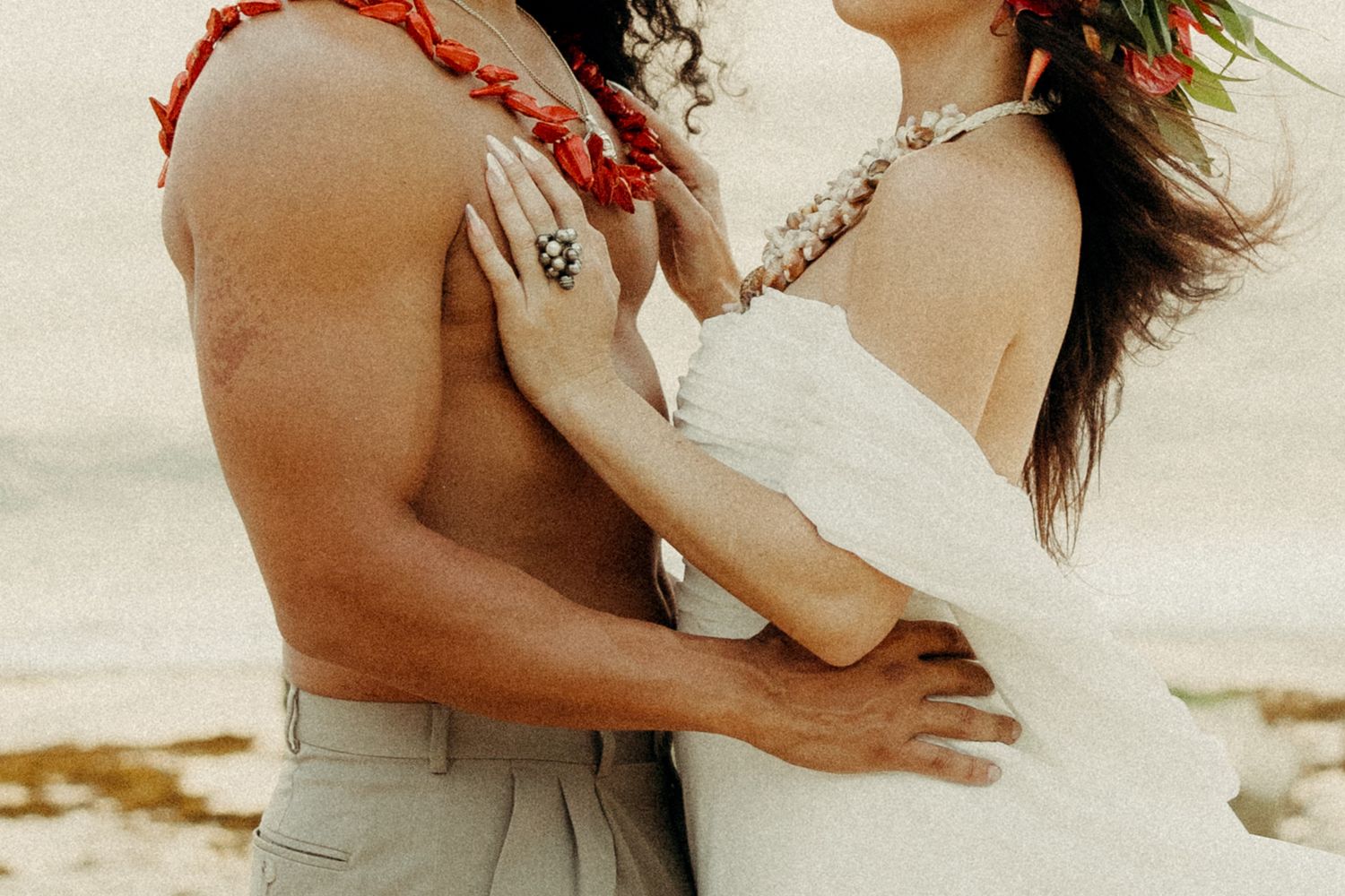 Couple in an intimate embrace on the beach, adorned with tropical floral leis.