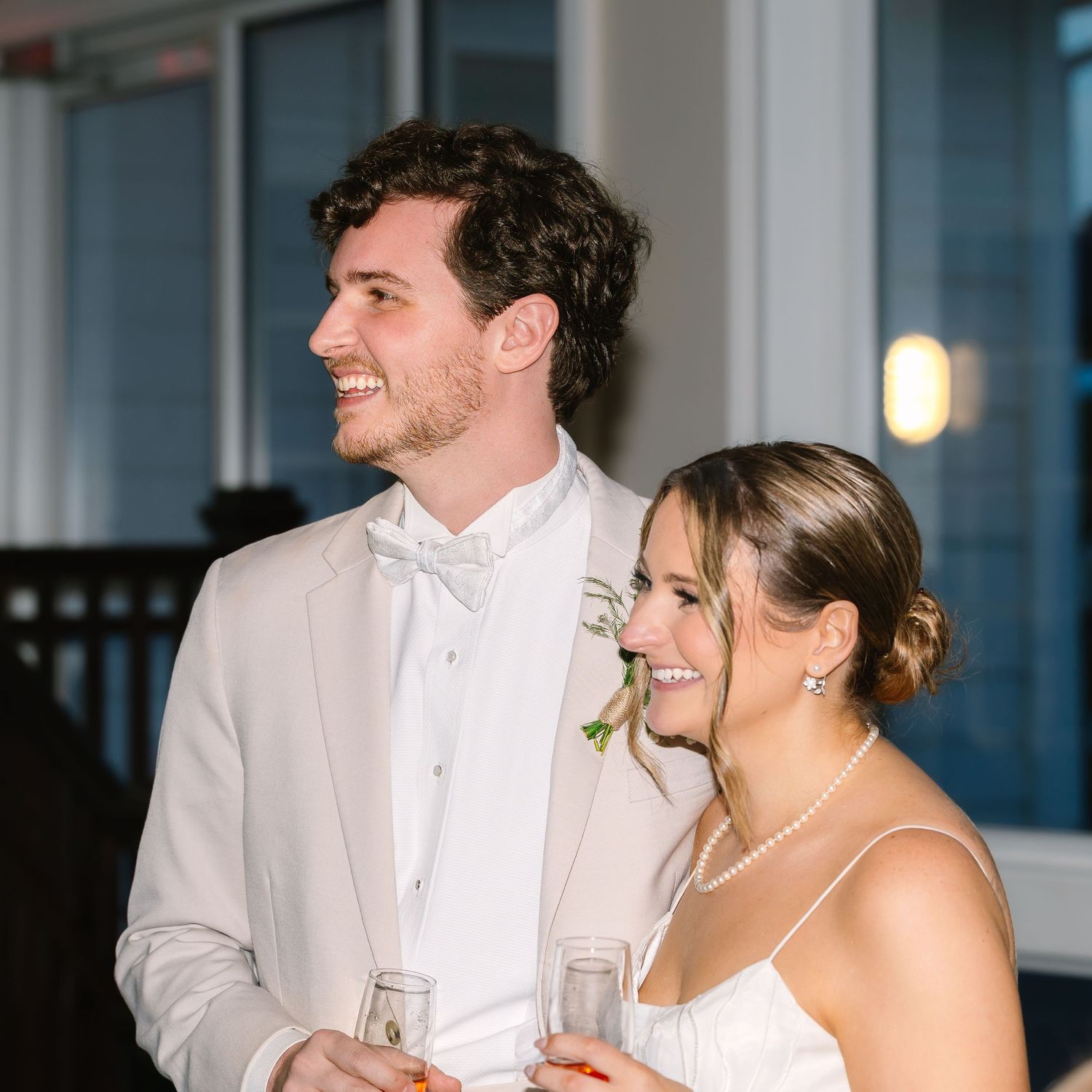 Smiling bride and groom in white wedding attire holding drinks during their reception celebration at Warwick Country Club in Rhode Island.
