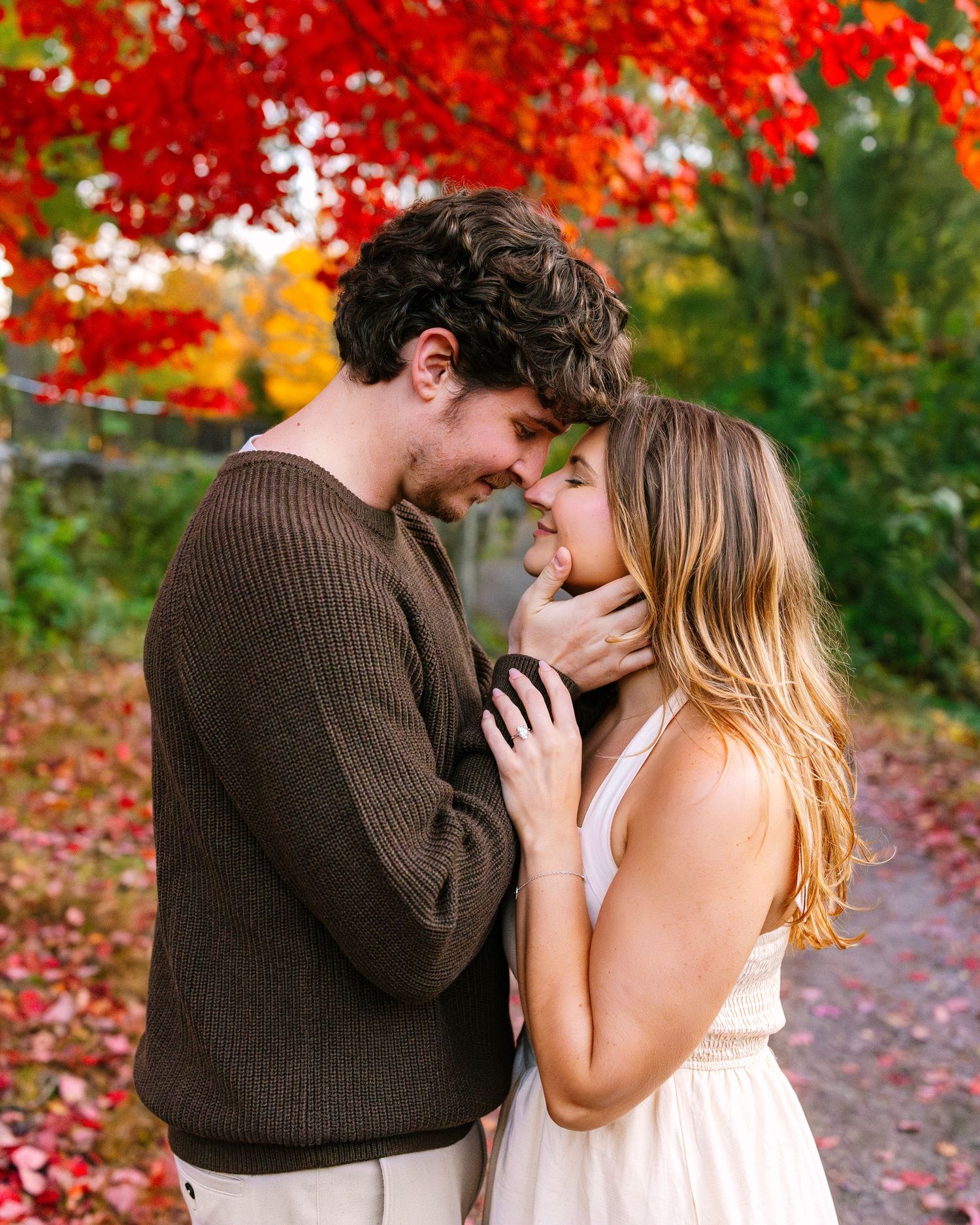A romantic couple embraces among vibrant red autumn foliage in an outdoor fall setting for engagement photos in Boston Massachusetts