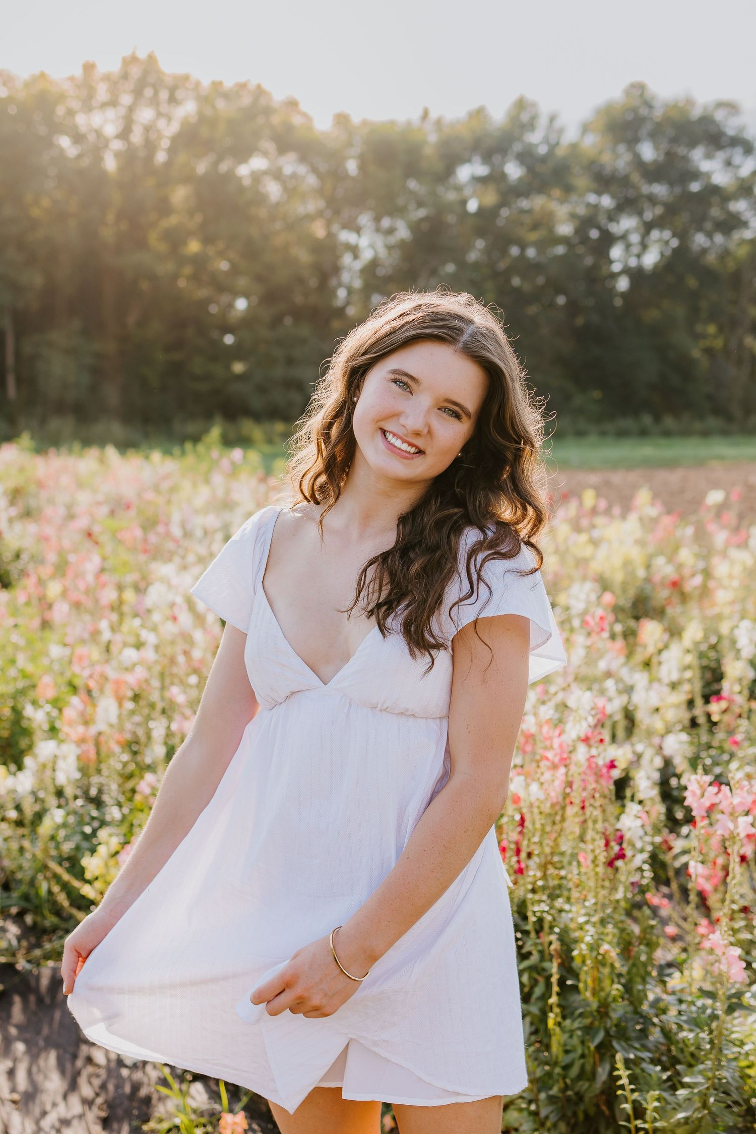 Young woman in white dress smiling in a colorful wildflower field during golden hour sunset.