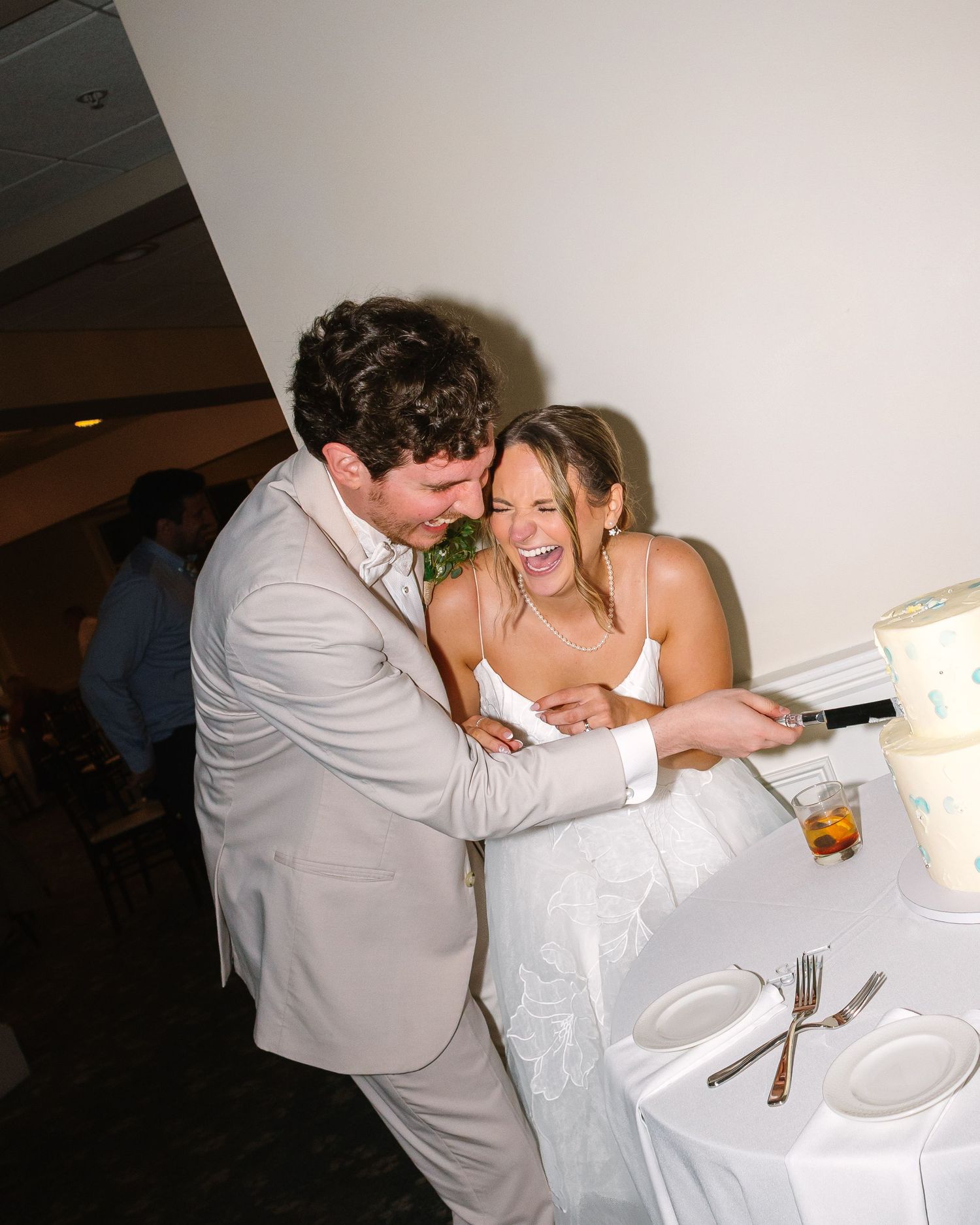 Joyful bride laughing with groom as they cut their wedding cake together at the reception.