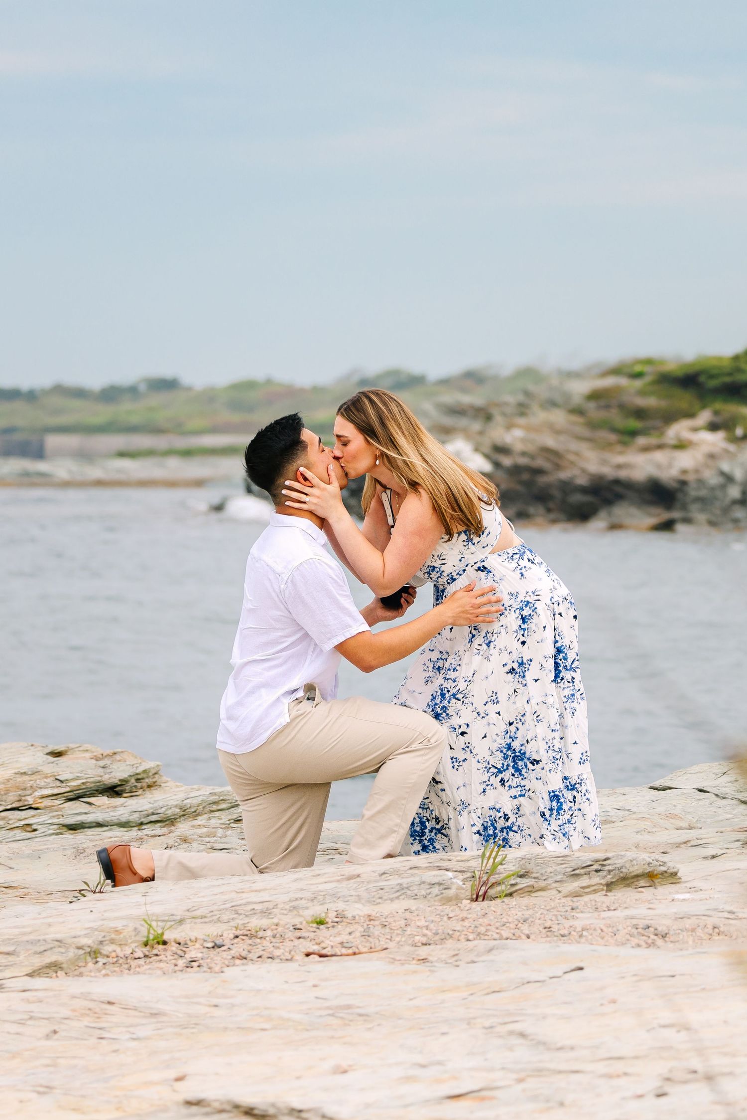 A man proposes to his fiancé on rocky cliffs by the ocean on Ocean Drive in Newport Rhode Island