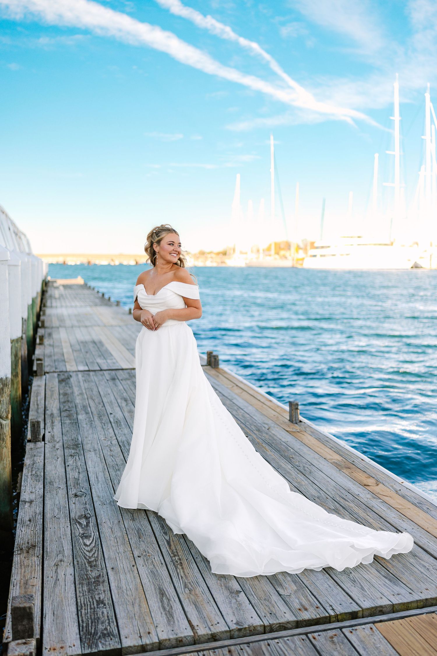 A bride in a flowing white dress twirls gracefully on a wooden dock by the ocean at sunset at The Regatta Place in Newport Rhode Island
