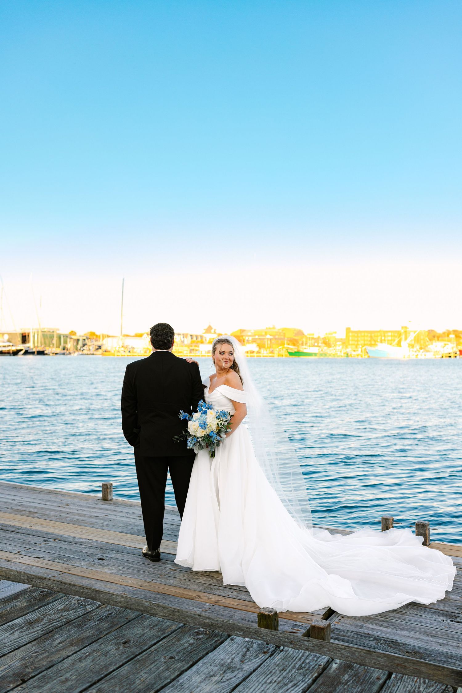 A bride and groom pose editorially by the ocean at sunset golden hour for couples portraits at wedding venue The Regatta Place in Newport RI