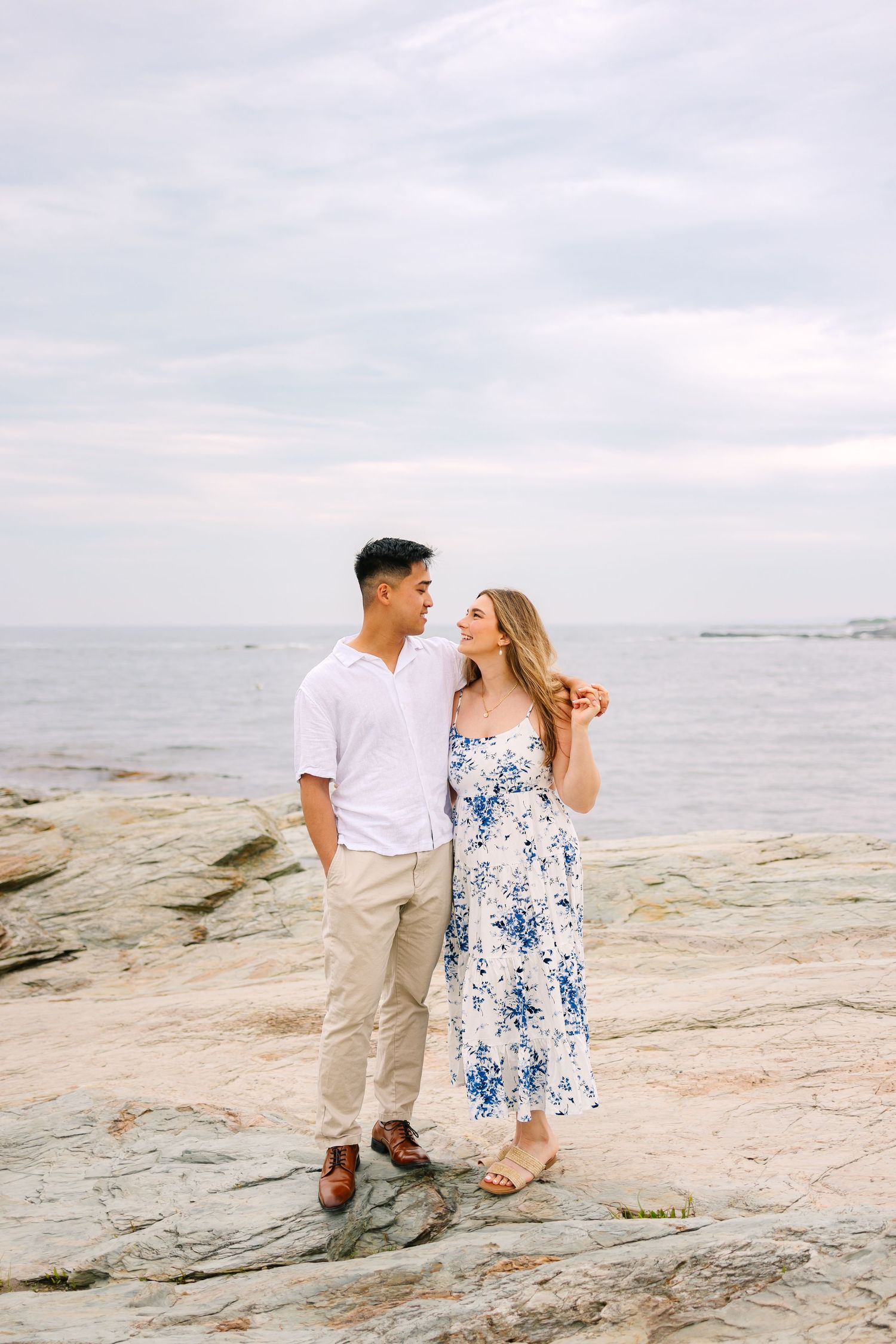 Couple standing on rocky shoreline for engagement photos gazing at each other by the sea on Ocean Drive in Newport Rhode Island