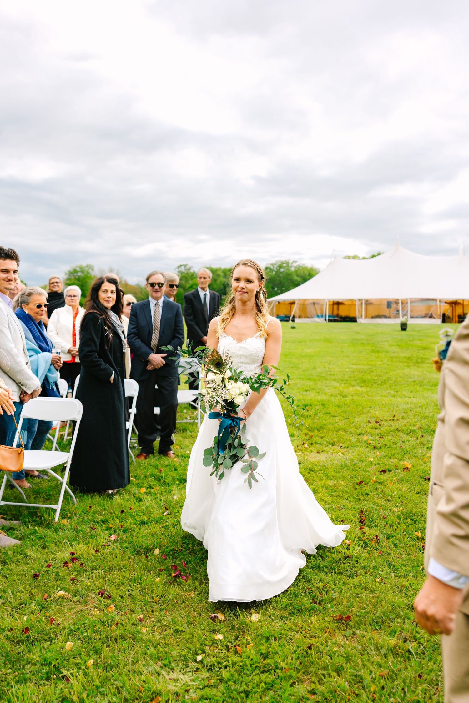 Festive wedding guests gather outdoors on a green lawn under cloudy skies at a reception celebration.