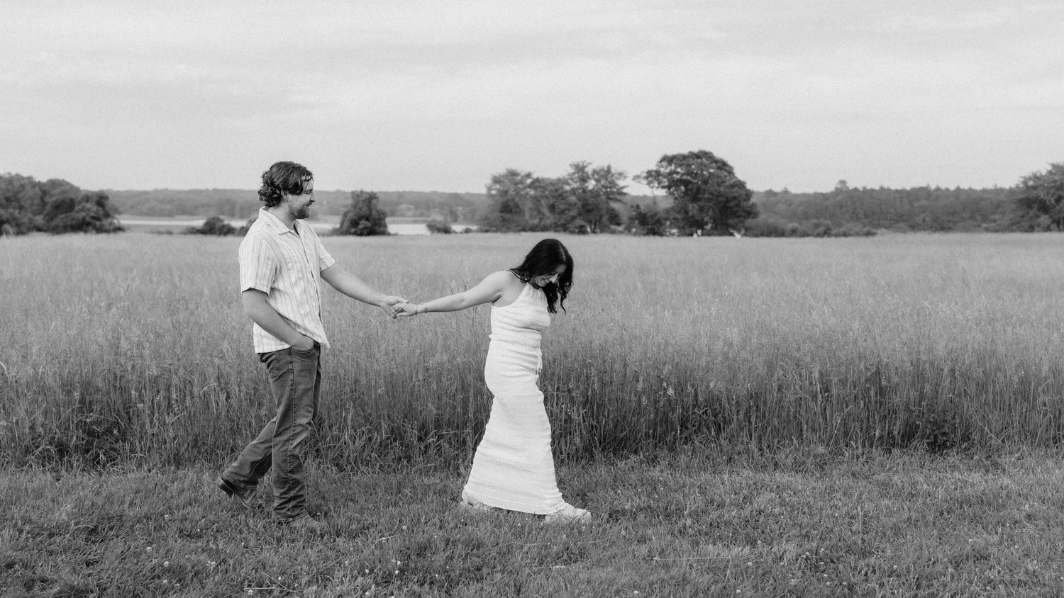 Black and white photo of couple holding hands in an open countryside field.