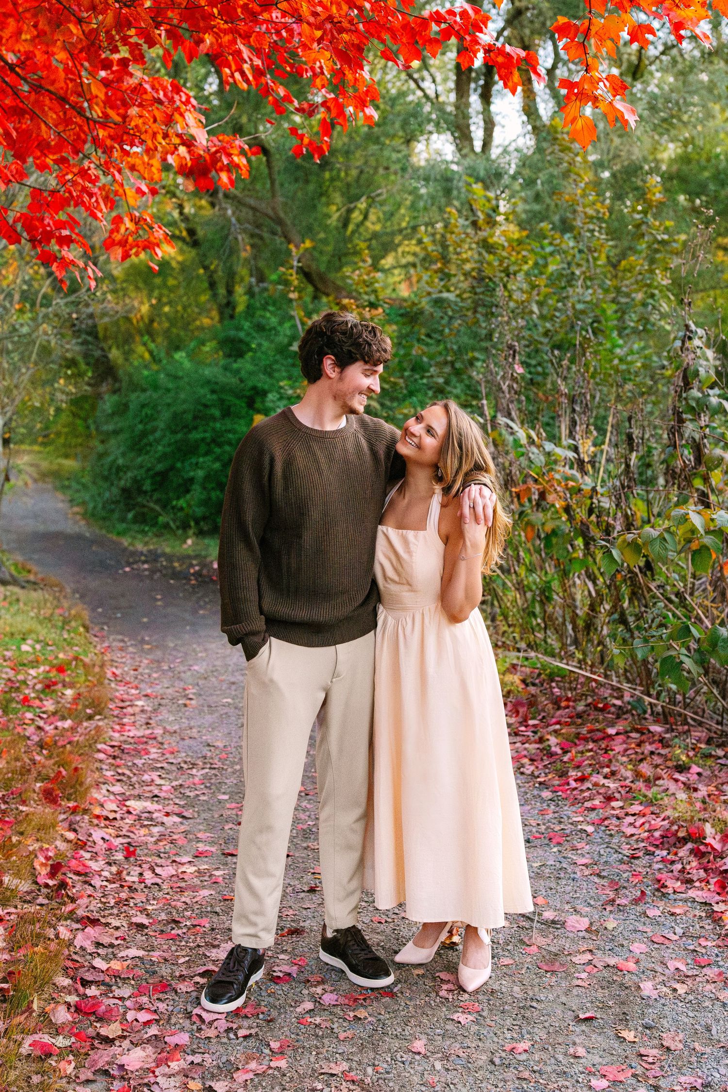 A couple shares romantic moments on a fall path covered in vibrant red maple leaves and autumn foliage at Arnold Arboretum in Boston MA