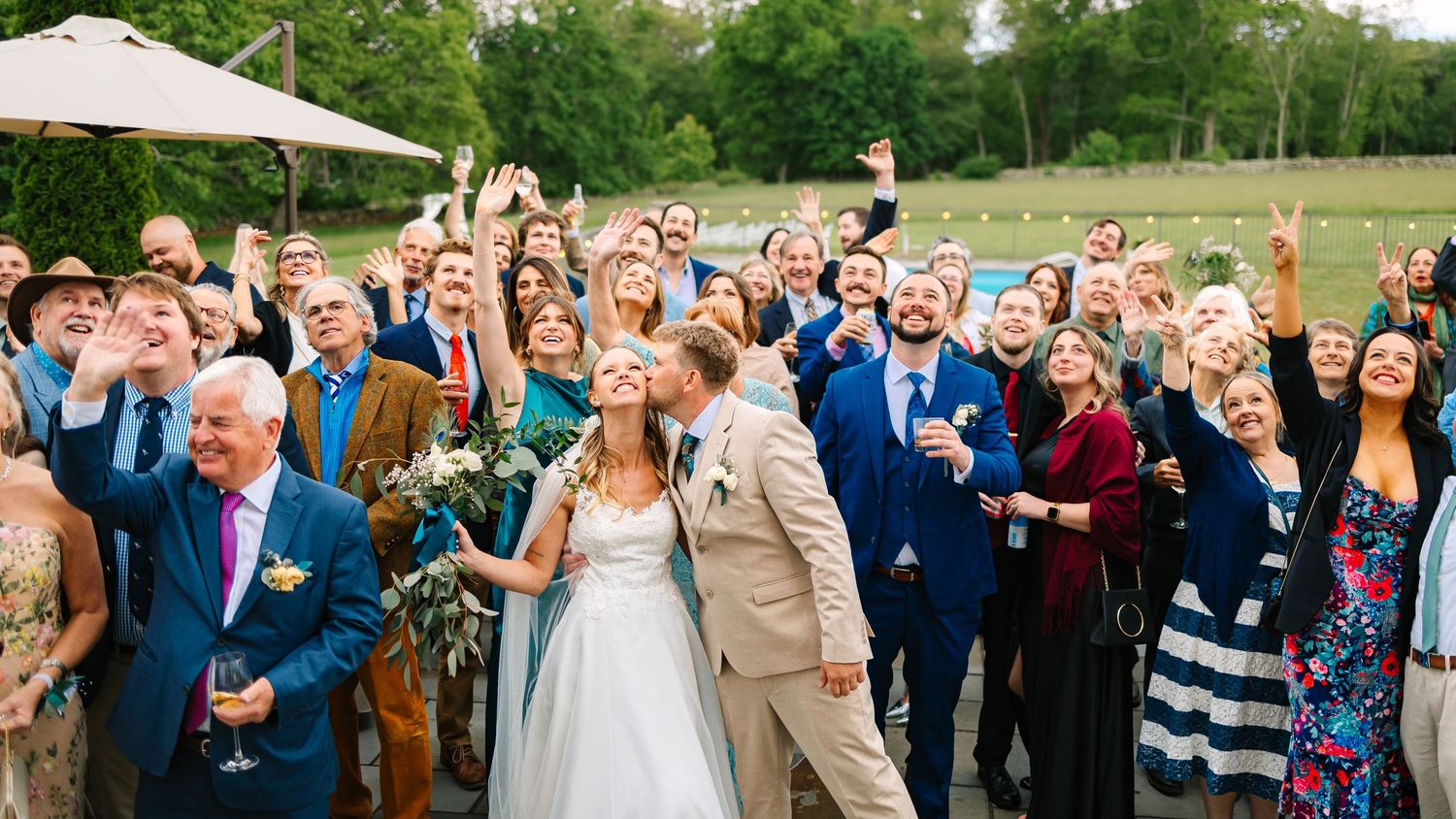 Wedding guests celebrate and cheer during an outdoor garden ceremony on a sunny summer day.