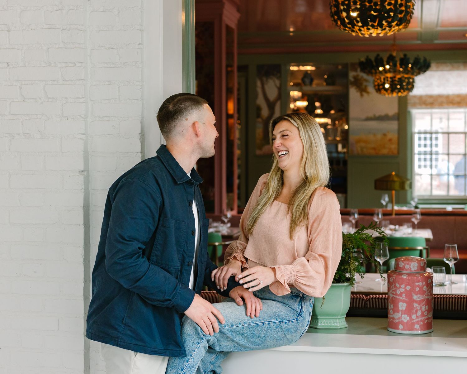 Joyful couple smiling and chatting while seated at a charming restaurant during engagement photos.