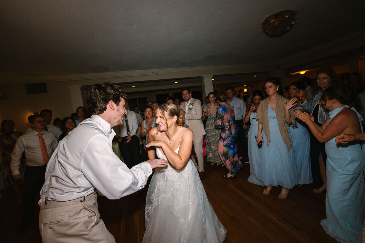 A bride and groom dance joyfully with guests celebrating on a lively wedding reception dance floor.
