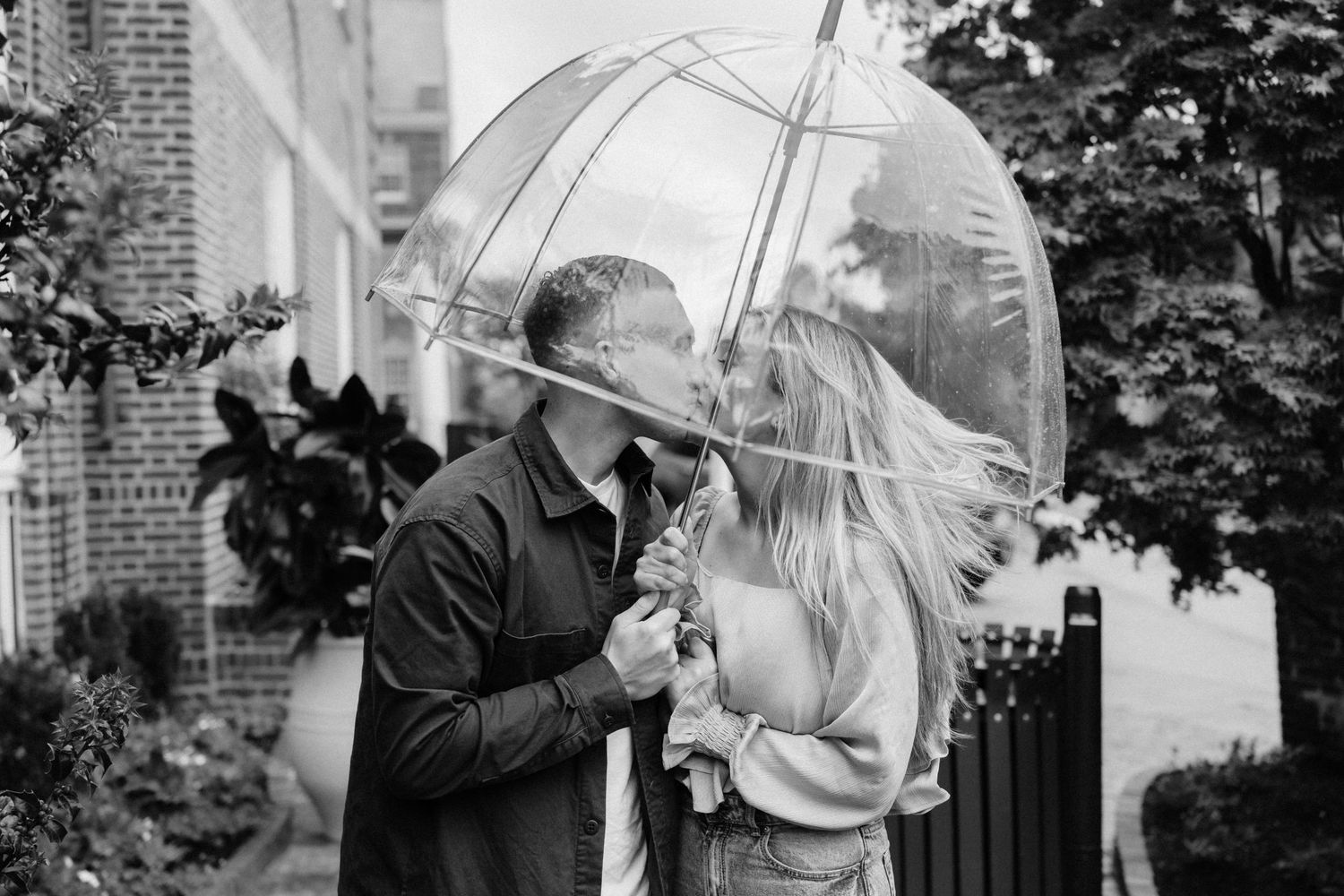 Romantic couple kissing under a clear umbrella on a windy day in black and white.