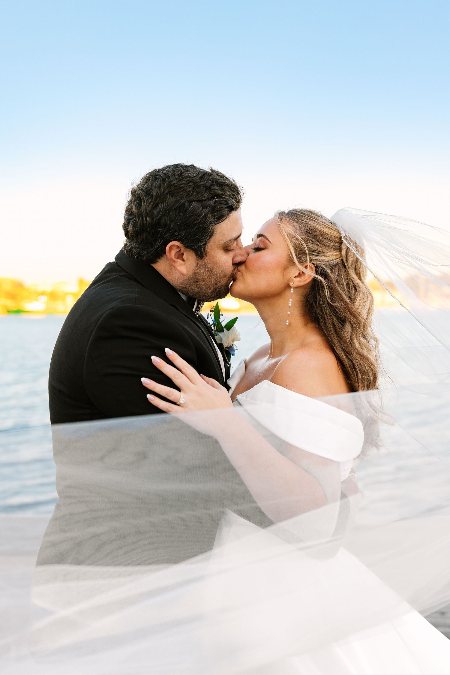 A romantic bride and groom couples portrait with a windswept veil kiss at sunset golden hour at The Regatta Place in Newport, Rhode Island